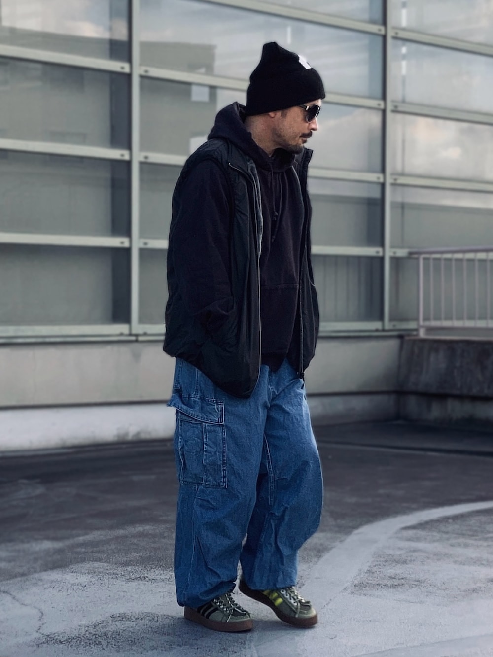 ブラック系のパーカー、ブラック系のベスト、ブルー系のカーゴパンツを着用したメンズの冬コーディネートの2枚目の写真