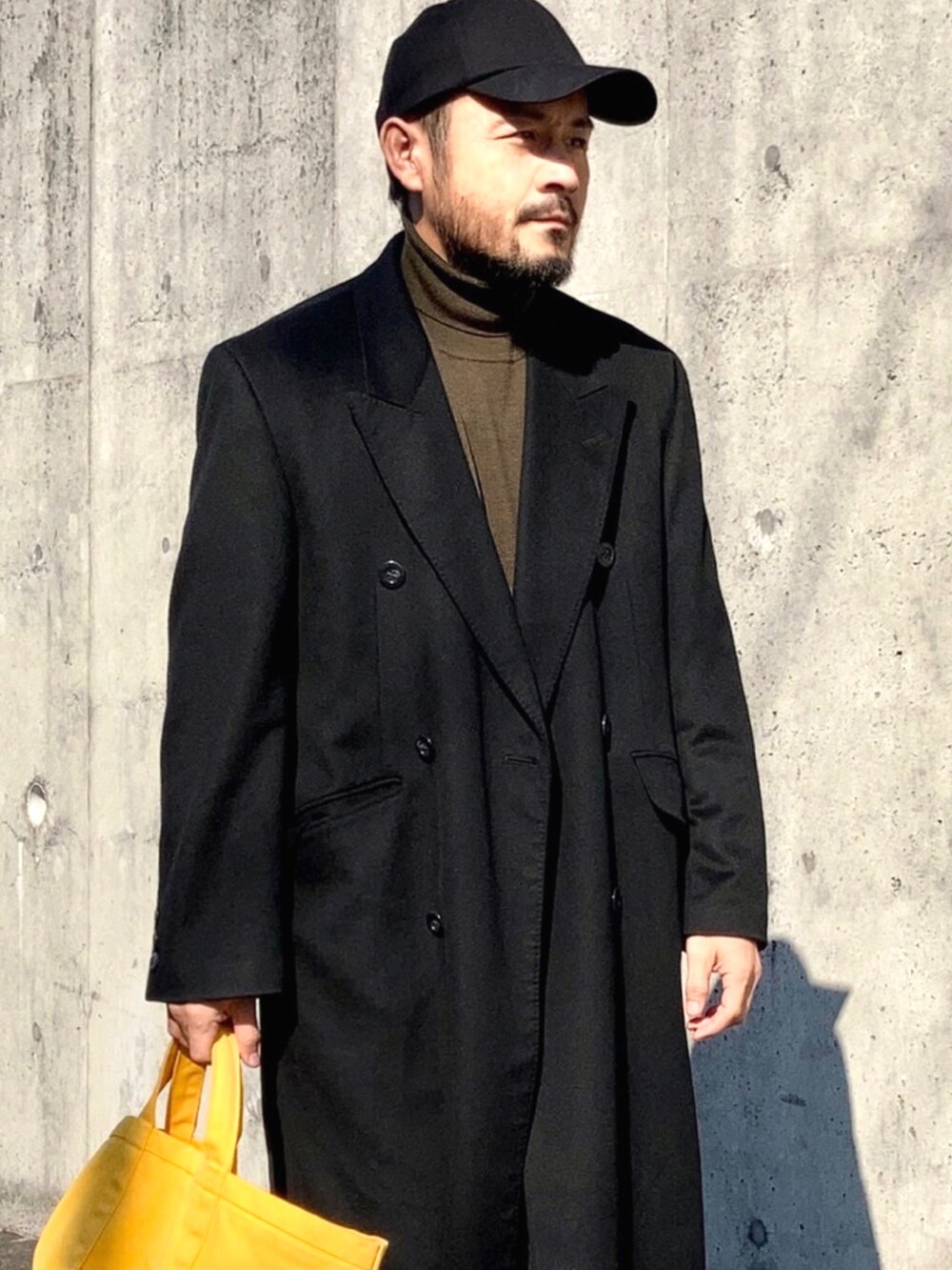 ブラック系のチェスターコート、ブルー系のデニムパンツ、ブラウン系のドレスシューズを着用したメンズの秋コーディネートの3枚目の写真