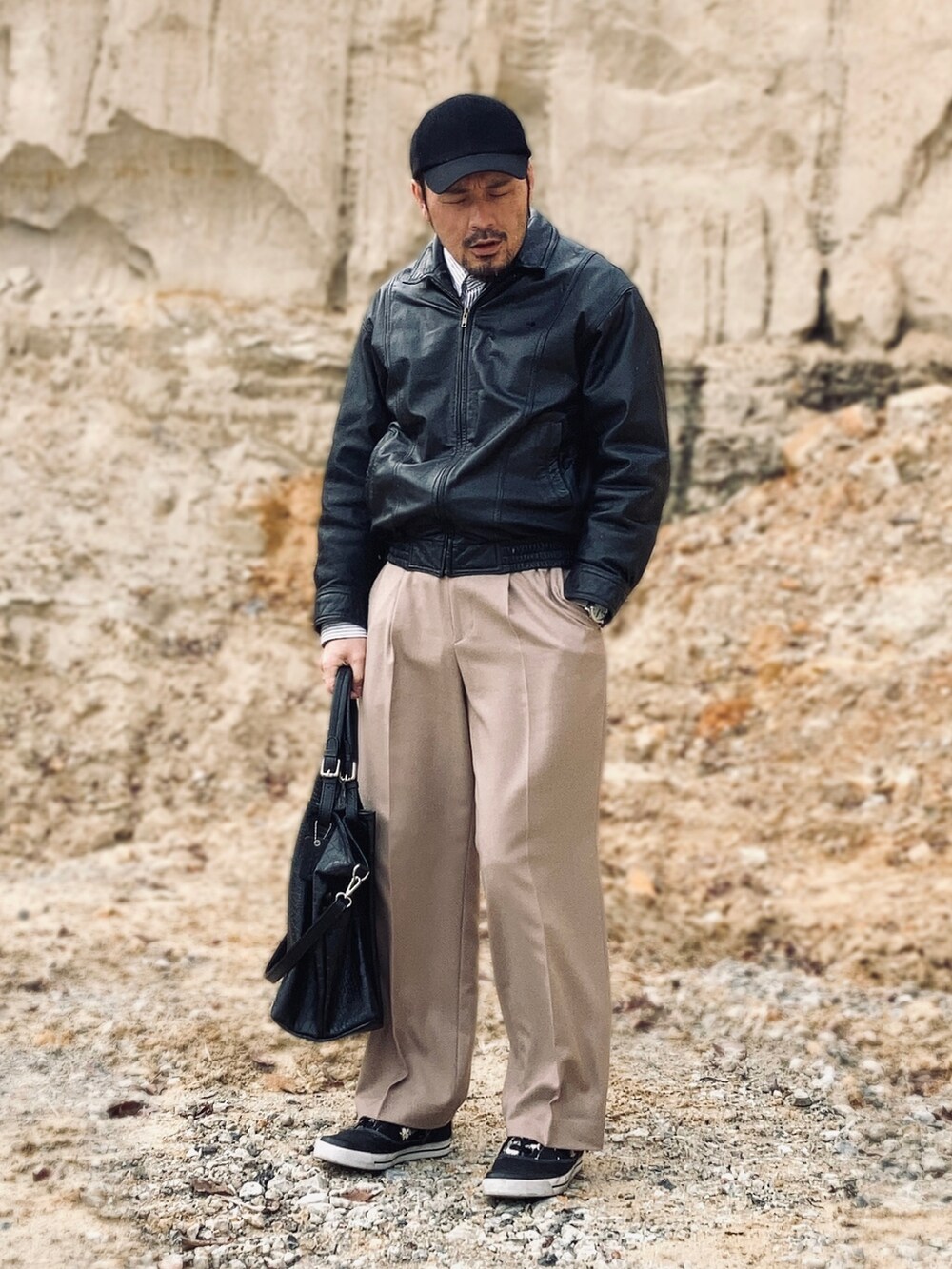 ブラック系のブルゾン、ベージュ系のスラックス、ブラック系のスニーカーを着用したメンズの春コーディネートの3枚目の写真