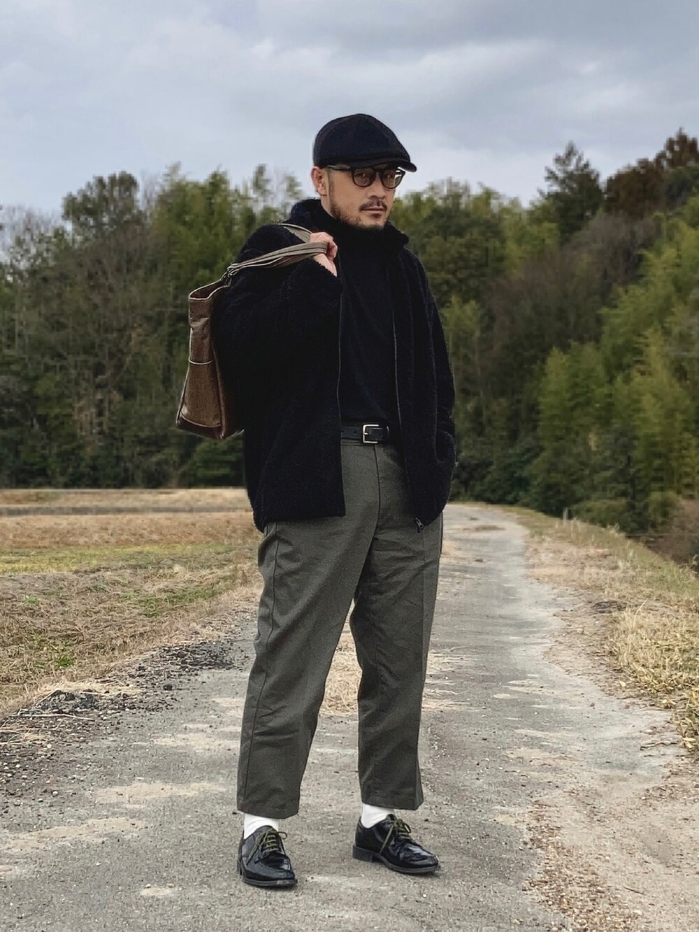 ブラック系のニット/セーター、ブラック系のその他アウター、グリーン系のチノパンツを着用したメンズの冬コーディネートの3枚目の写真