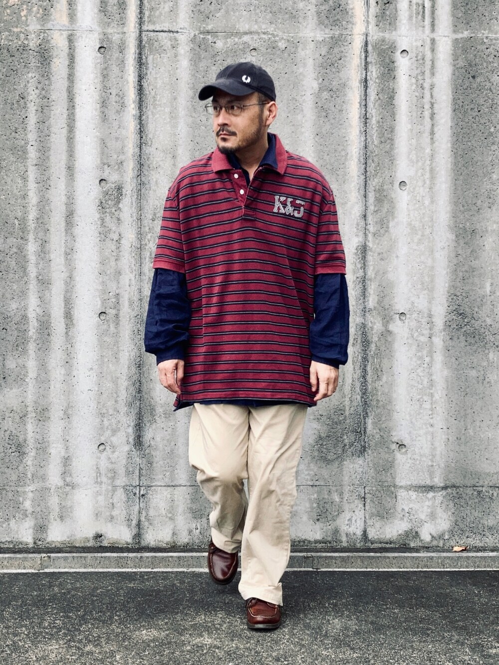 レッド系のポロシャツ、ベージュ系のチノパンツ、ブラウン系のモカシン/デッキシューズを着用したメンズの秋コーディネートの2枚目の写真