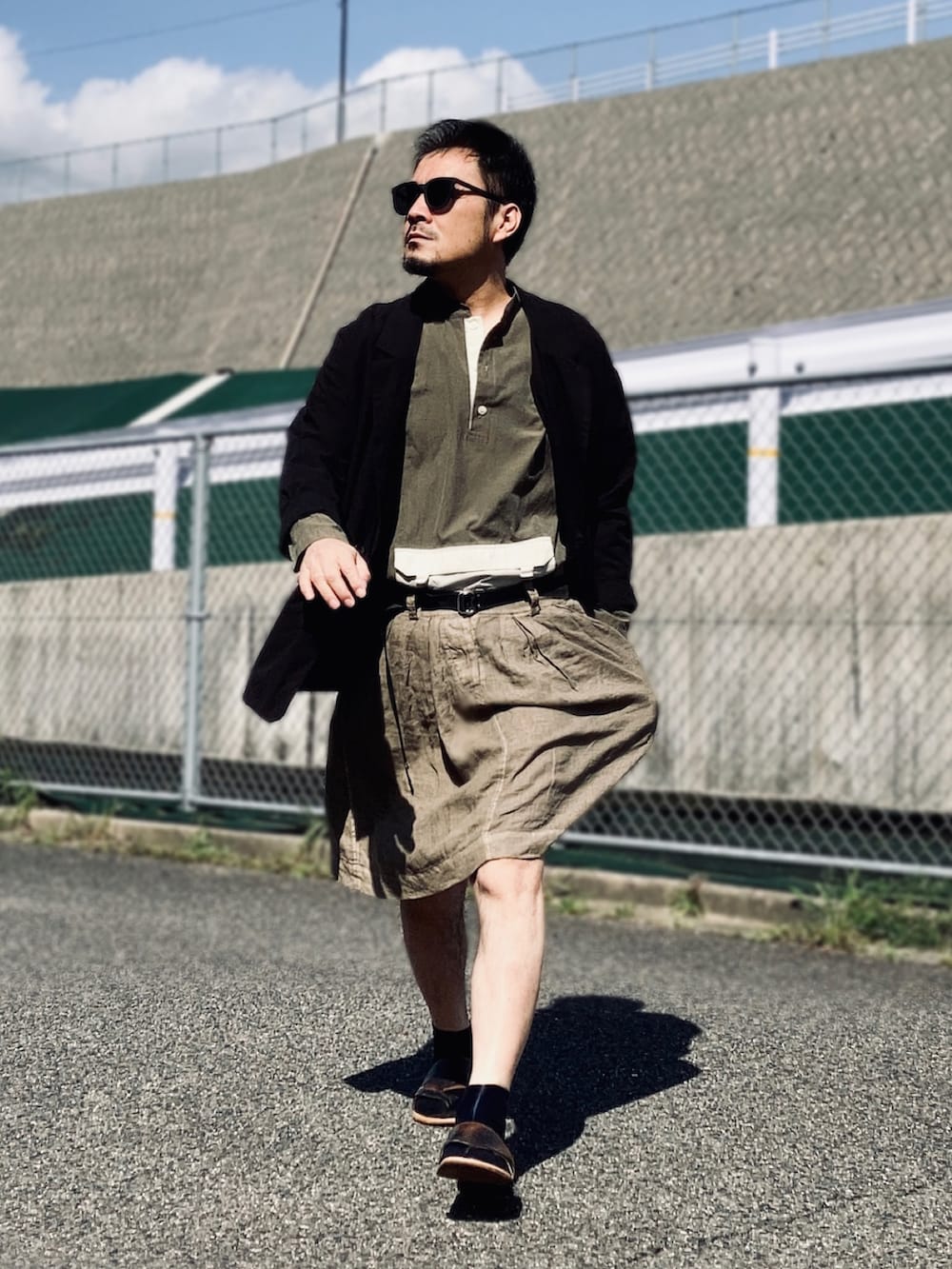 グリーン系のトップス、ブラック系のテーラードジャケット、グリーン系のスカートを着用したメンズの春コーディネートの2枚目の写真