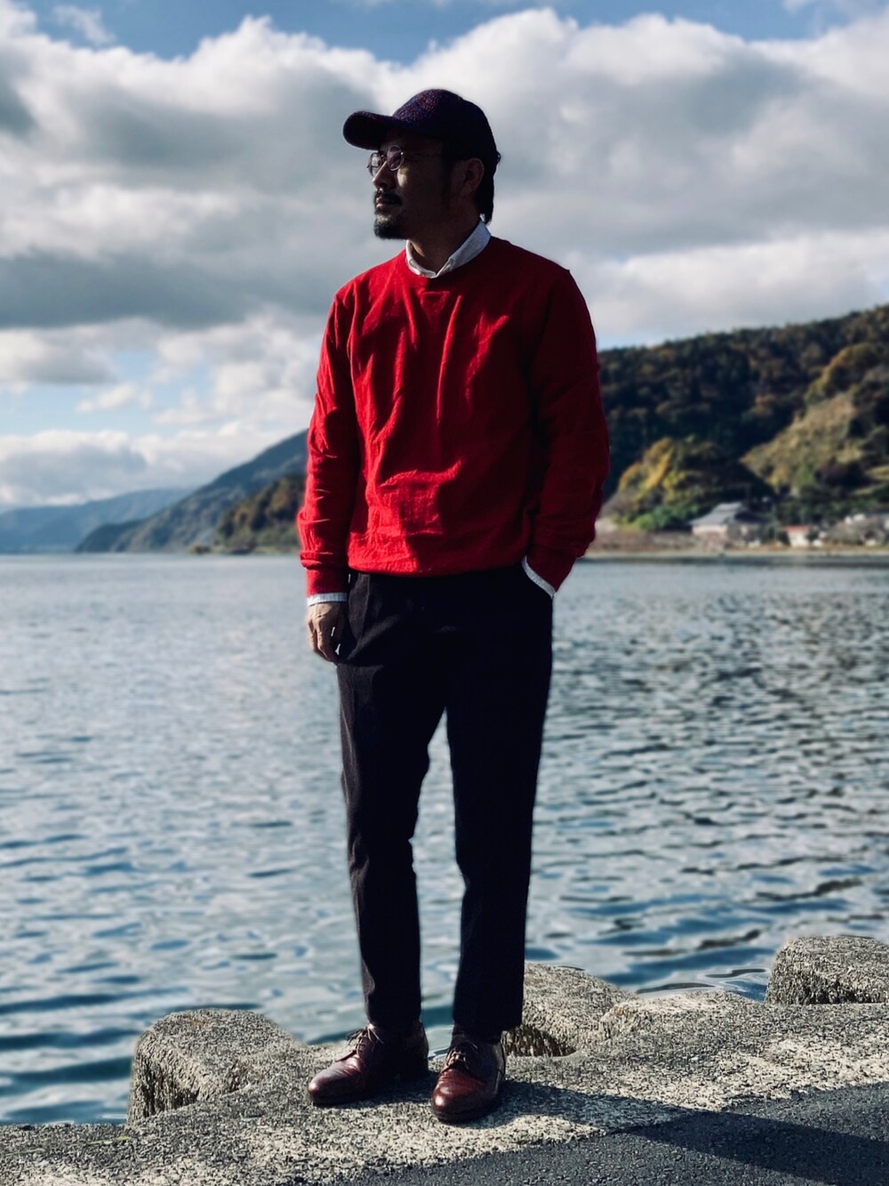 レッド系のニット/セーター、ホワイト系のシャツ/ブラウス、ベージュ系のトレンチコートを着用したメンズの秋コーディネートの3枚目の写真