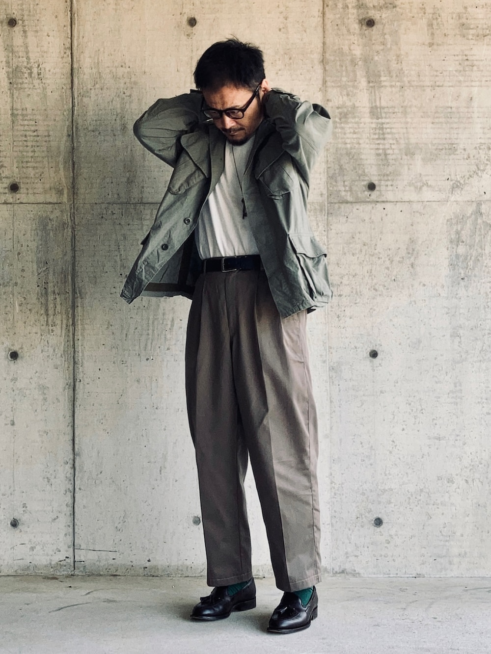 ホワイト系のTシャツ/カットソー、グリーン系のミリタリージャケット、グレー系のスラックスを着用したメンズの春コーディネートの2枚目の写真