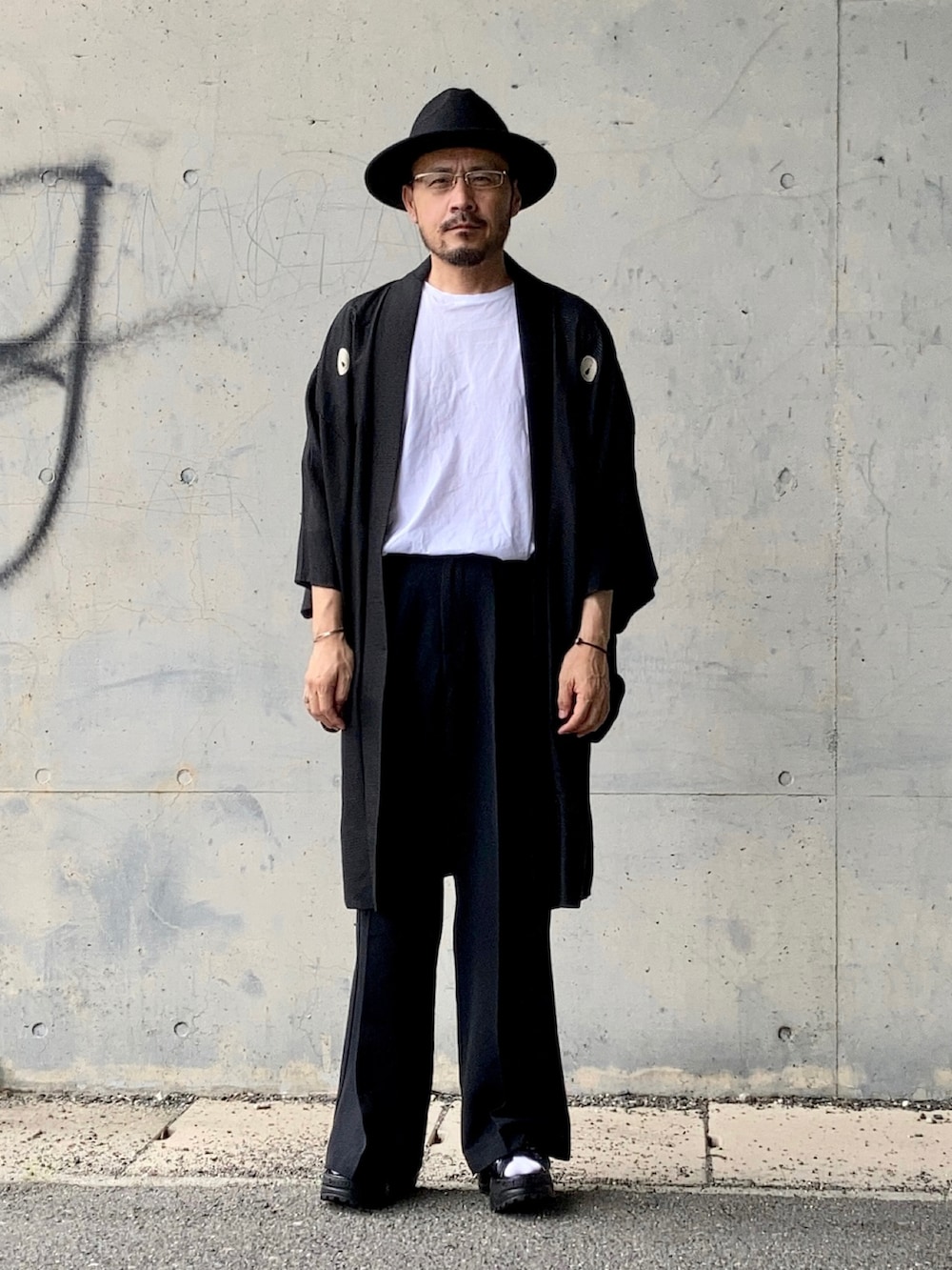 ホワイト系のTシャツ/カットソー、ブラック系のスラックス、ブラック系のサンダルを着用したメンズの夏コーディネートの2枚目の写真