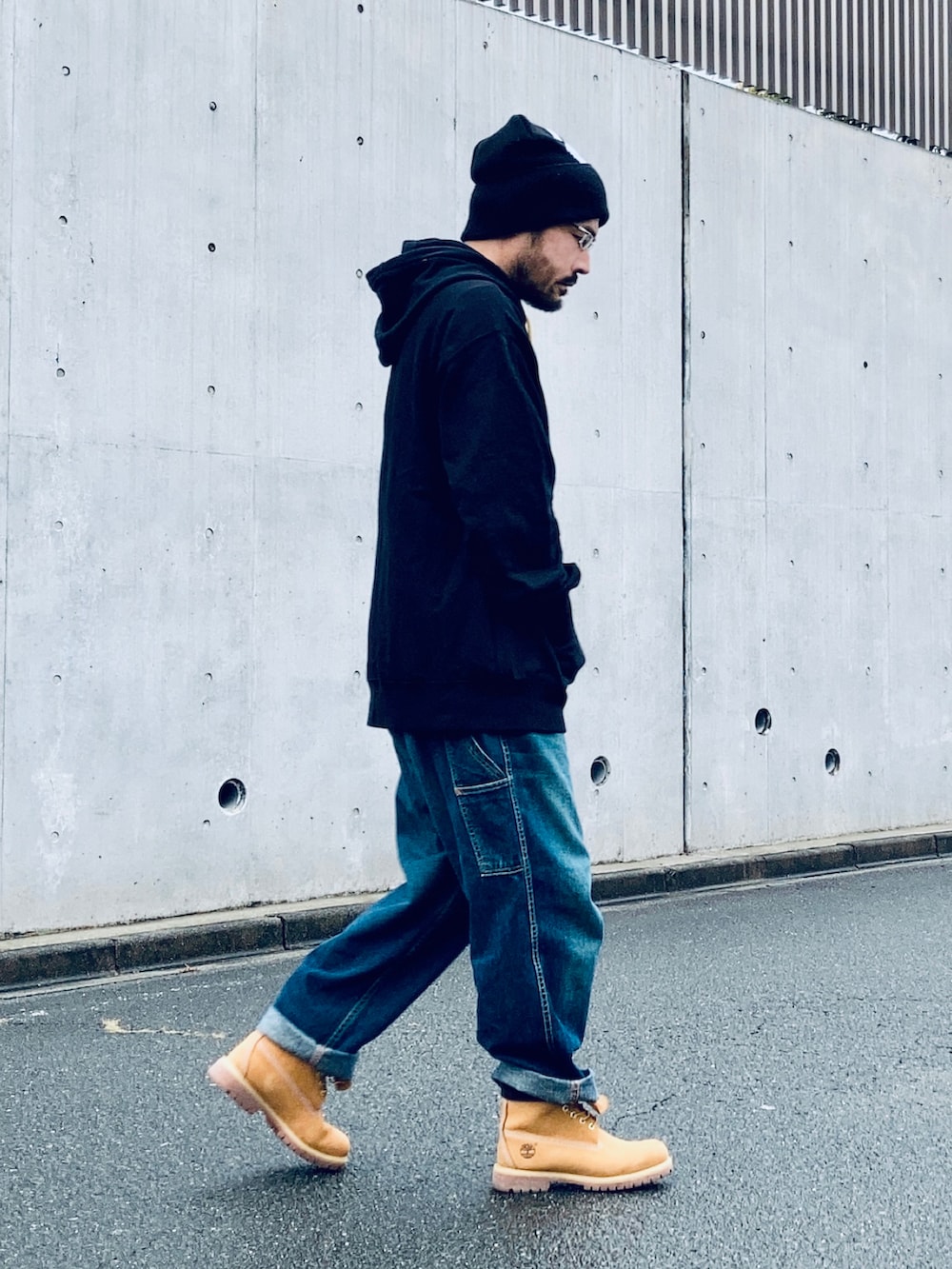 ブラック系のパーカー、ブルー系のデニムパンツ、イエロー系のブーツを着用したメンズの秋コーディネートの2枚目の写真