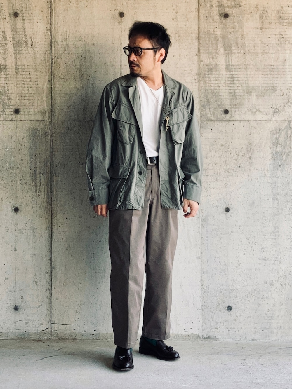 ホワイト系のTシャツ/カットソー、グリーン系のミリタリージャケット、グレー系のスラックスを着用したメンズの春コーディネートの3枚目の写真