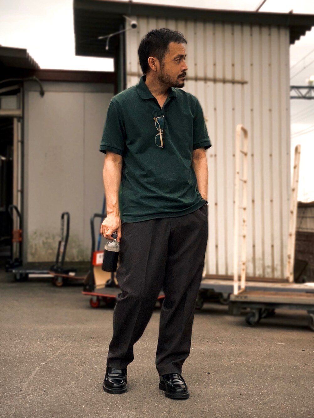 グリーン系のポロシャツ、グレー系のスラックス、ブラック系のローファーを着用したメンズの夏コーディネートの2枚目の写真