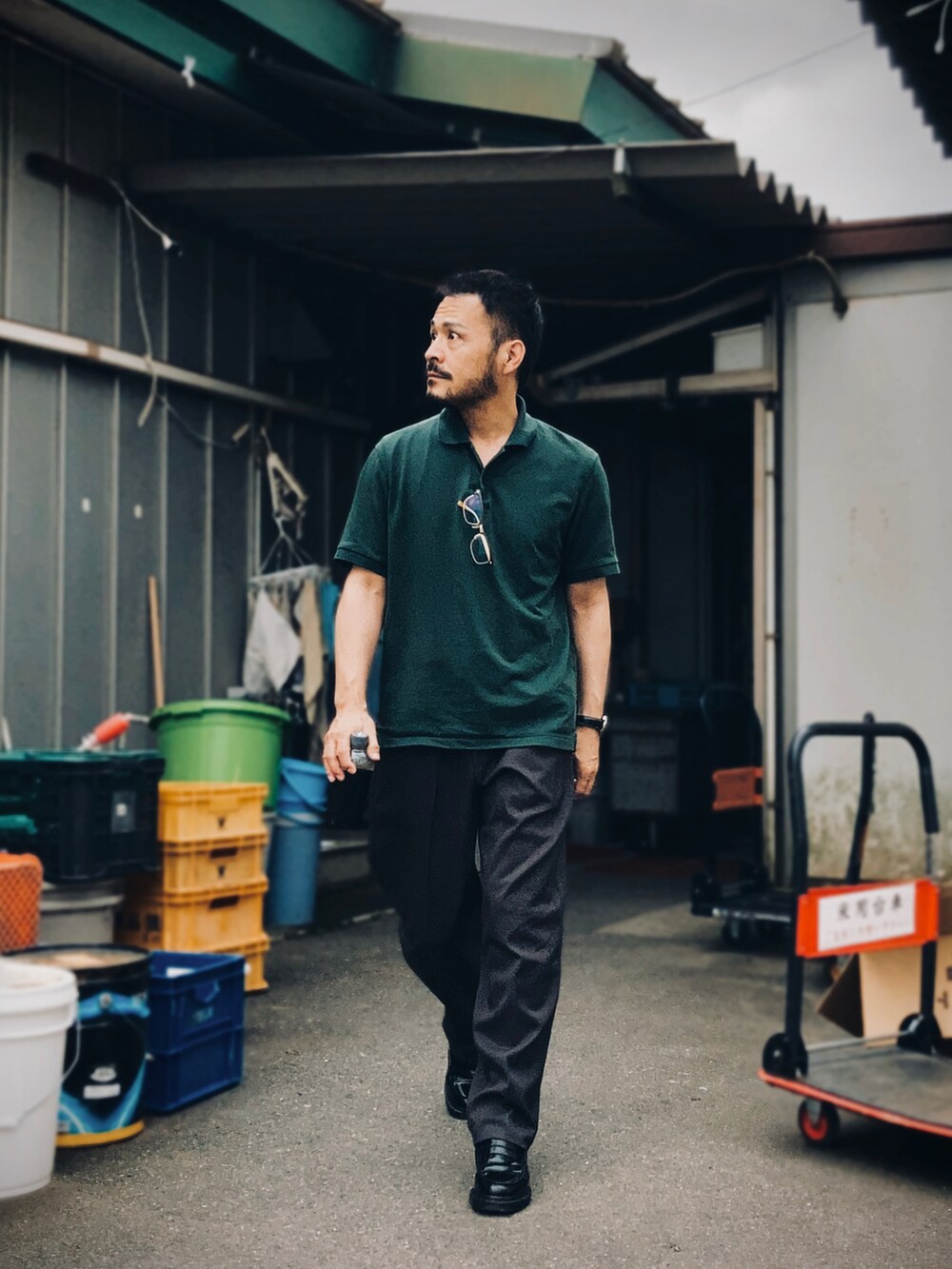 グリーン系のポロシャツ、グレー系のスラックス、ブラック系のローファーを着用したメンズの夏コーディネートの3枚目の写真