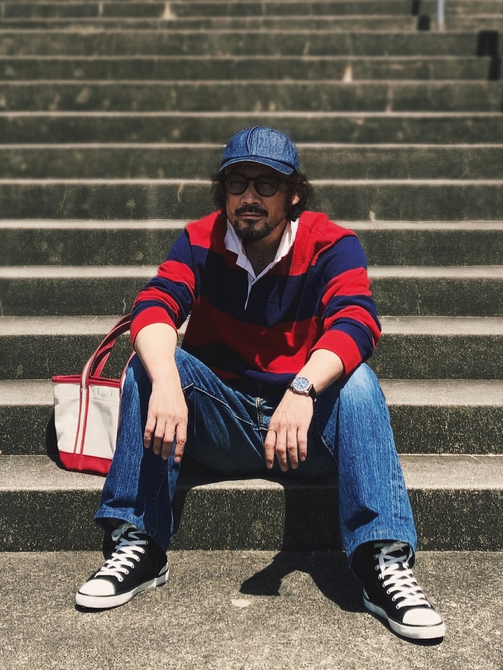 レッド系のポロシャツ、ブルー系のデニムパンツ、ブラック系のスニーカーを着用したメンズの春コーディネートの2枚目の写真