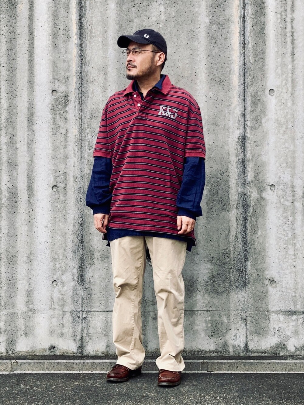 レッド系のポロシャツ、ベージュ系のチノパンツ、ブラウン系のモカシン/デッキシューズを着用したメンズの秋コーディネートの3枚目の写真
