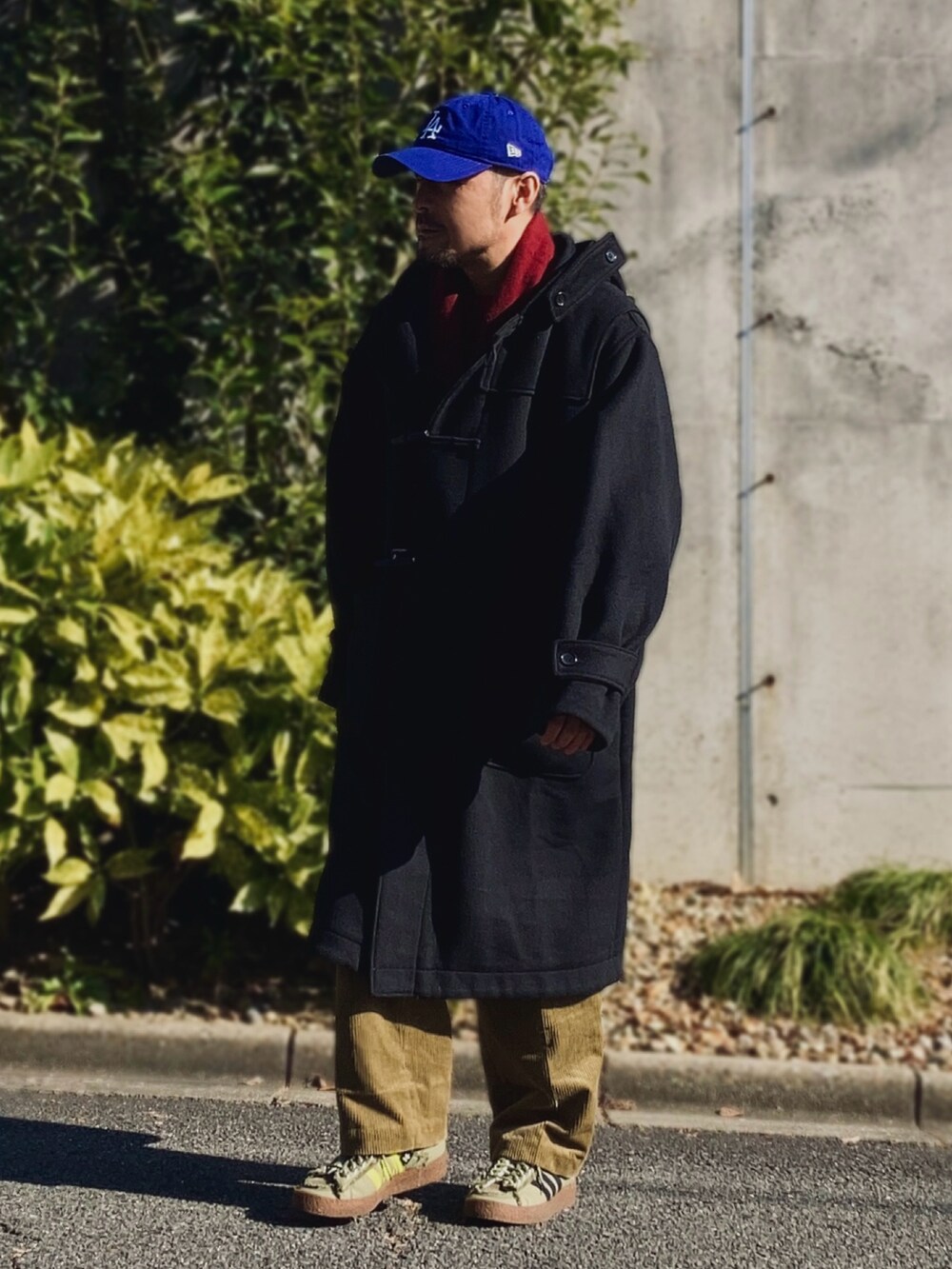 レッド系のニット/セーター、ブラック系のダッフルコート、ゴールド系のスラックスを着用したメンズの冬コーディネートの4枚目の写真