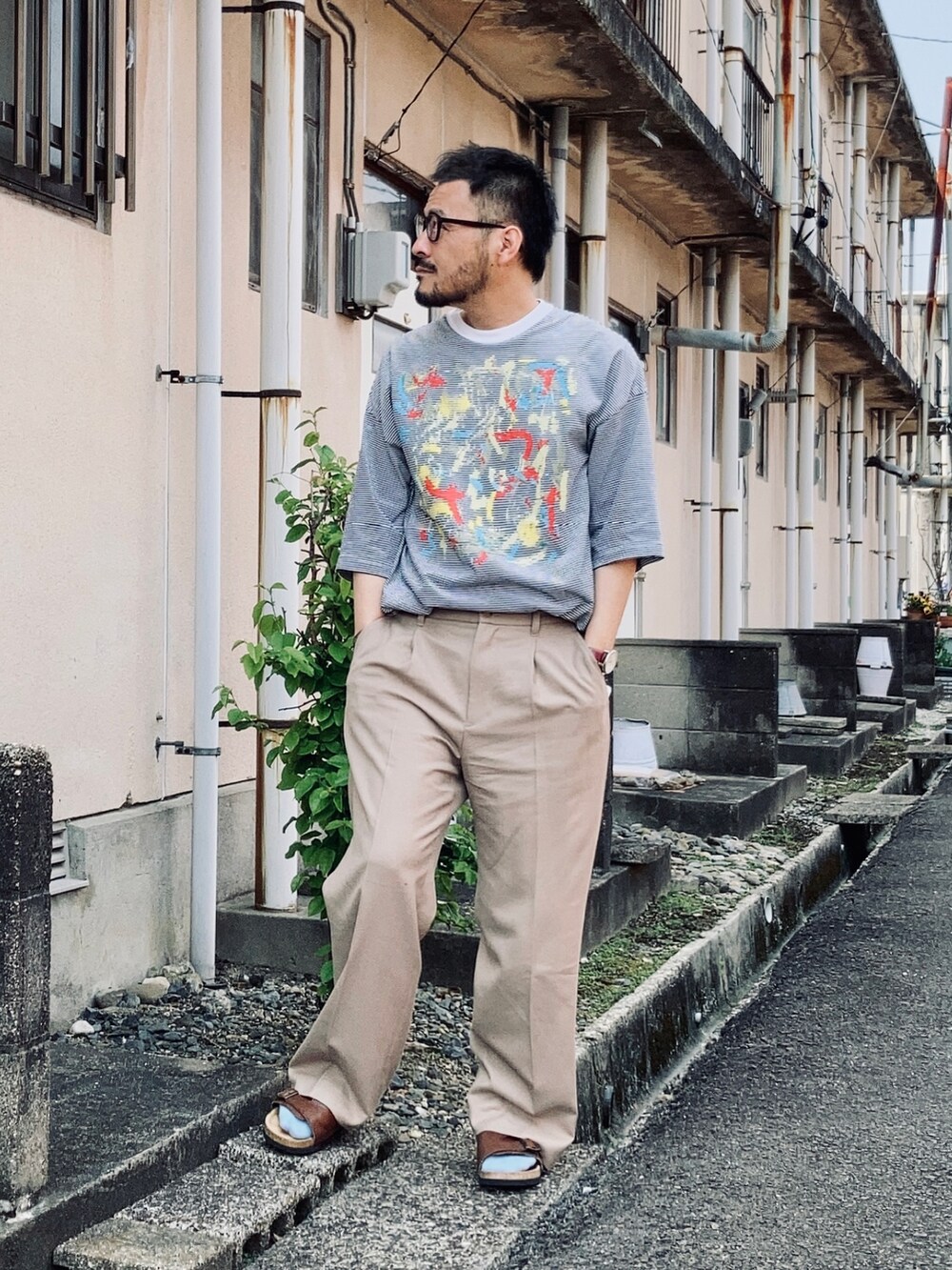 ホワイト系のTシャツ/カットソー、ベージュ系のスラックス、ブラウン系のサンダルを着用したメンズの春コーディネートの3枚目の写真