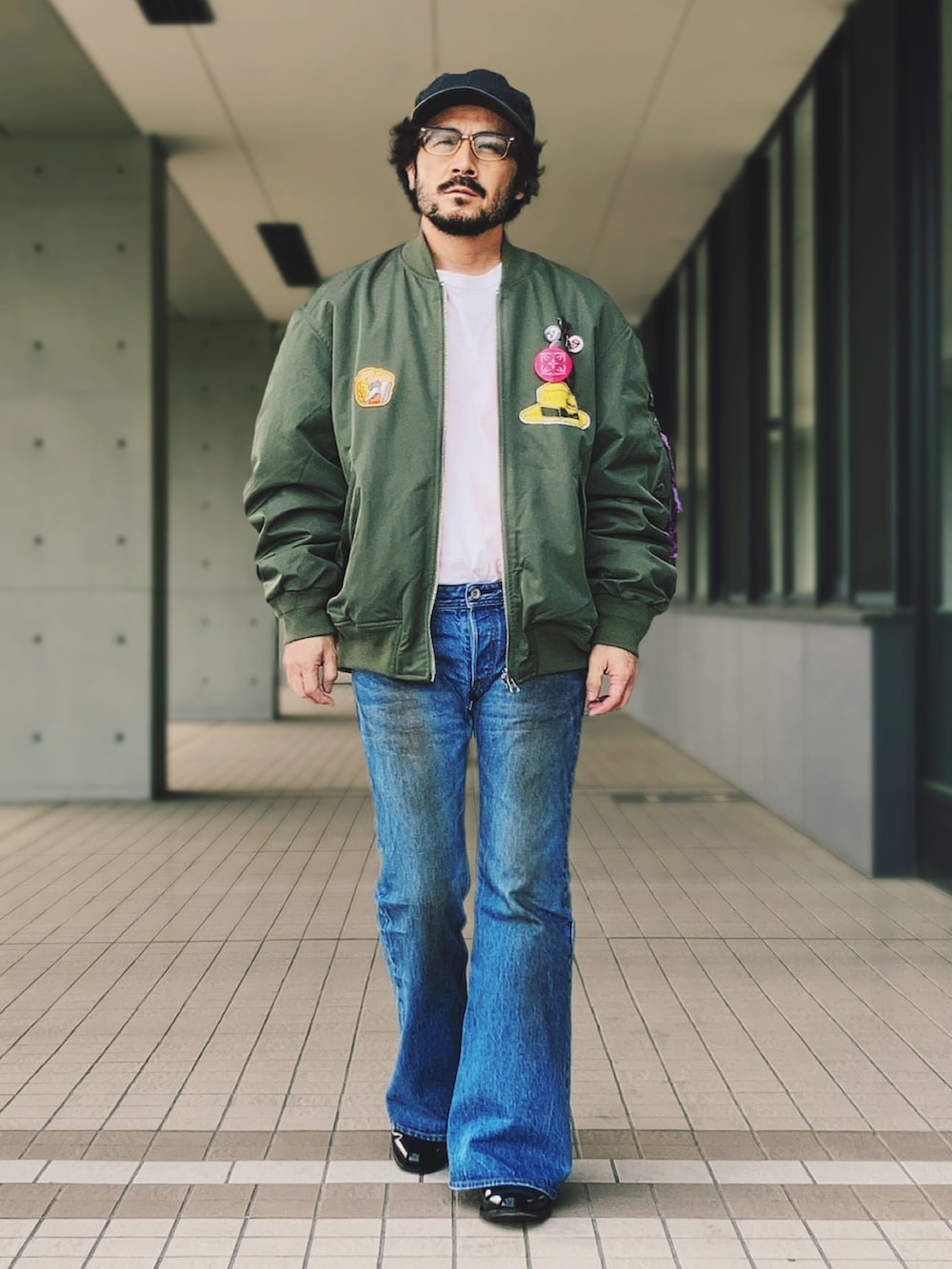 グリーン系のMA-1、ブルー系のデニムパンツ、ブラック系のブーツを着用したメンズの春コーディネートの2枚目の写真