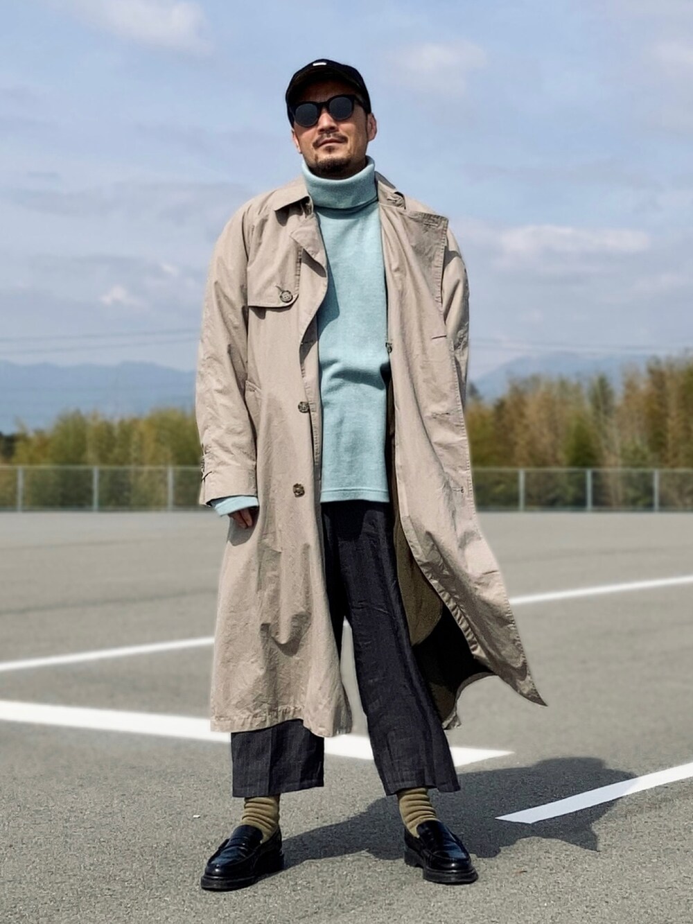 ブルー系のニット/セーター、ベージュ系のトレンチコート、グレー系のスラックスを着用したメンズの春コーディネートの4枚目の写真