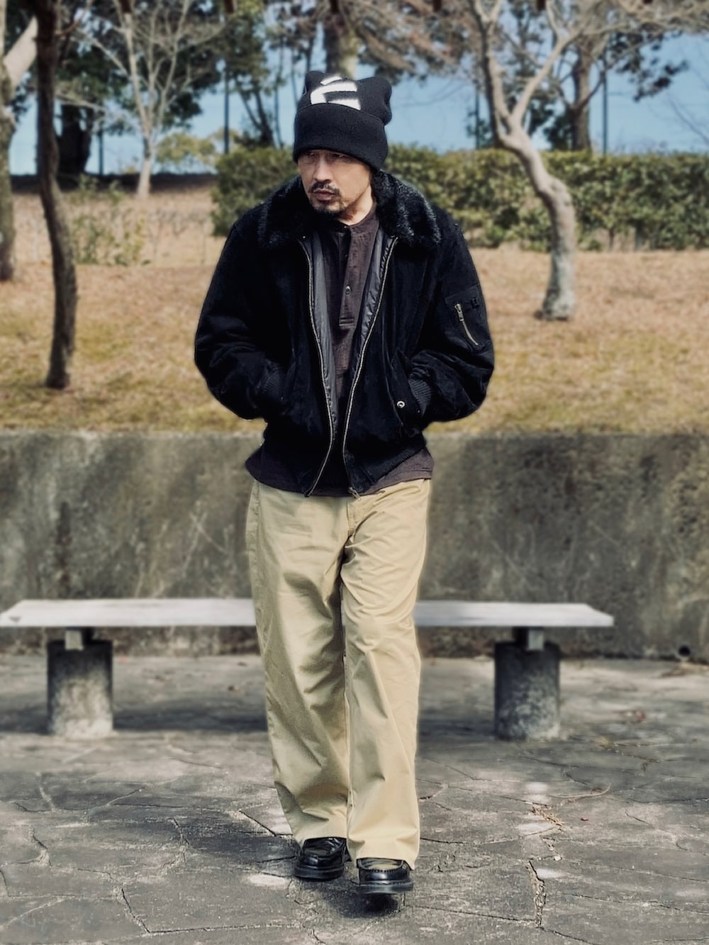 ブラック系のブルゾン、ブラウン系のTシャツ/カットソー、ベージュ系のチノパンツを着用したメンズの冬コーディネートの2枚目の写真