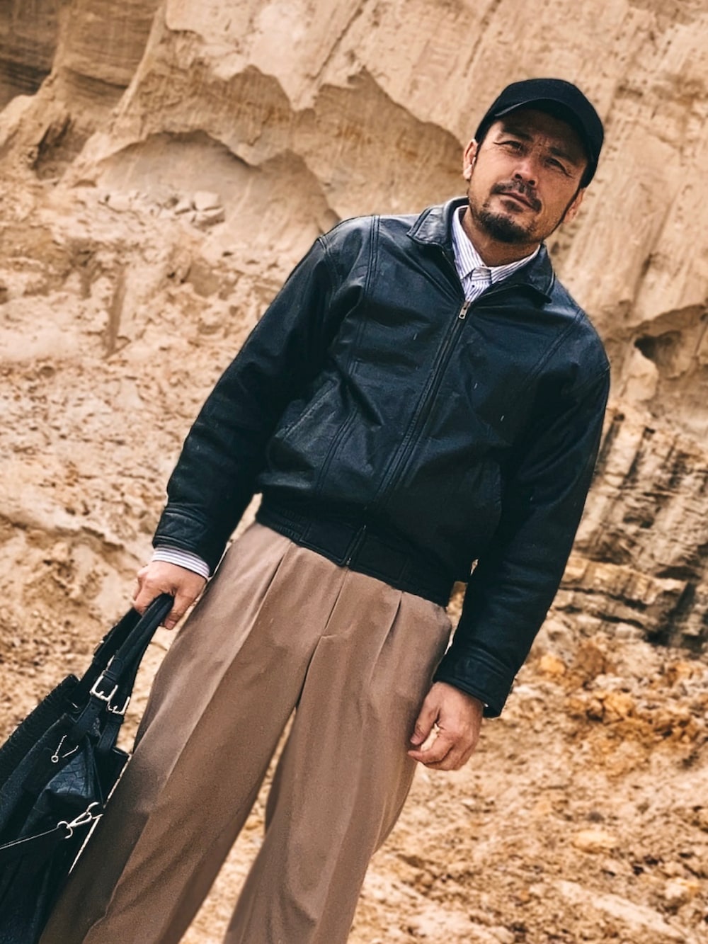 ブラック系のブルゾン、ベージュ系のスラックス、ブラック系のスニーカーを着用したメンズの春コーディネートの5枚目の写真