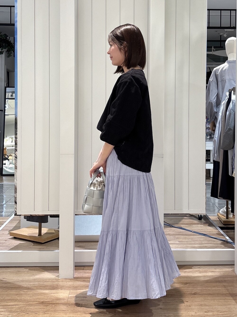 ブルー系のスカート、ブラック系のパンプス、シルバー系のトートバッグを着用したレディースの春コーディネートの2枚目の写真