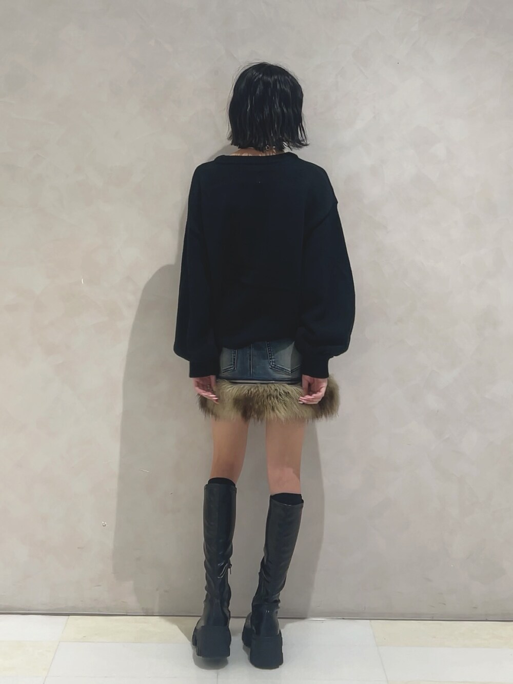 ブラック系のニット/セーター、ブルー系のスカート、ブラック系のブーツを着用したレディースの秋コーディネートの3枚目の写真