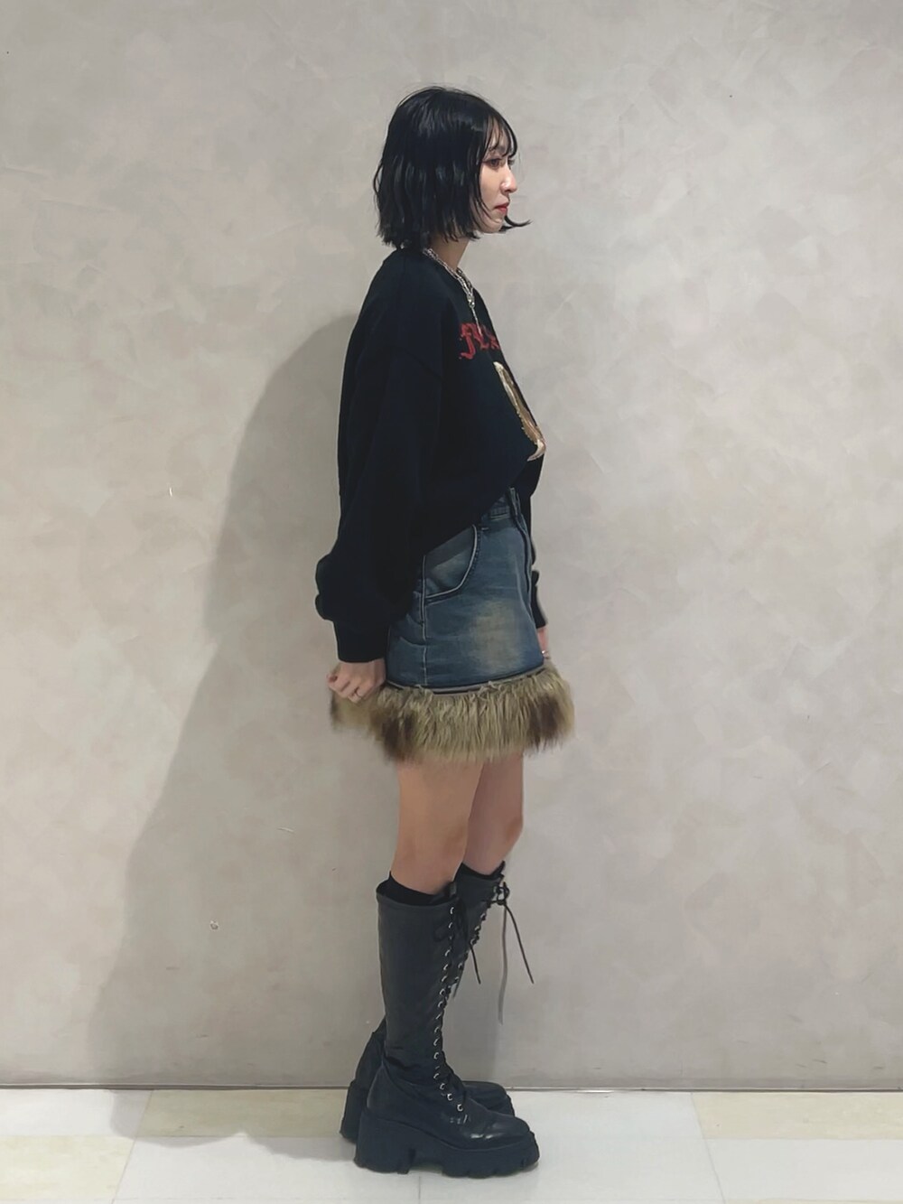 ブラック系のニット/セーター、ブルー系のスカート、ブラック系のブーツを着用したレディースの秋コーディネートの2枚目の写真