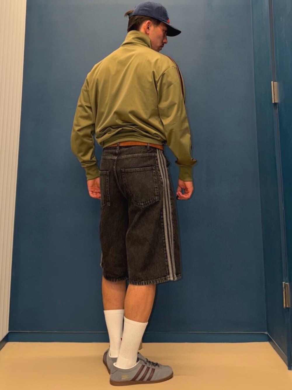 グリーン系のジャージ、グレー系のスニーカー、ブラック系のデニムパンツを着用したメンズの春コーディネートの2枚目の写真