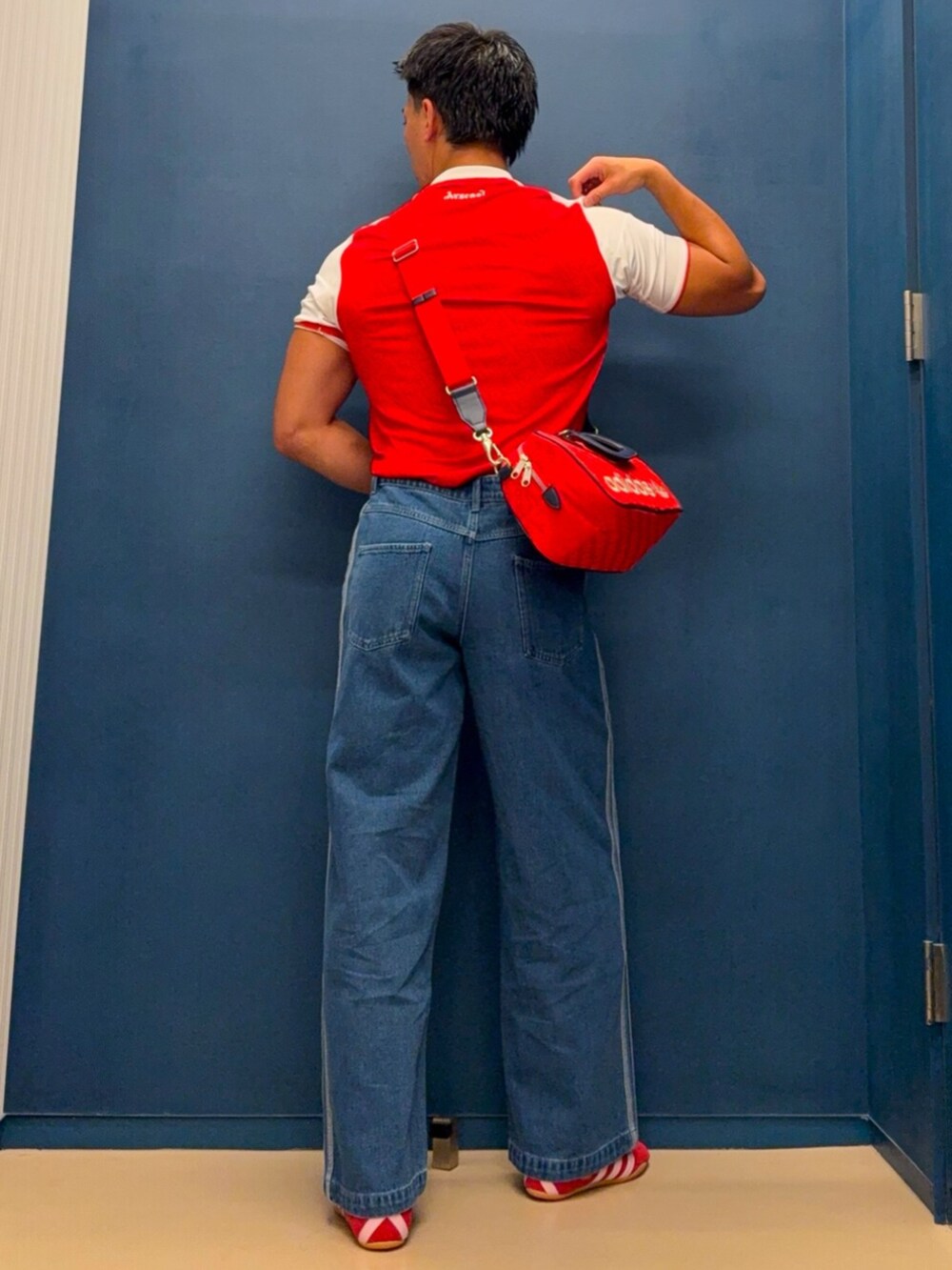 レッド系のTシャツ/カットソー、ブルー系のデニムパンツ、レッド系のハンドバッグを着用したメンズの夏コーディネートの2枚目の写真