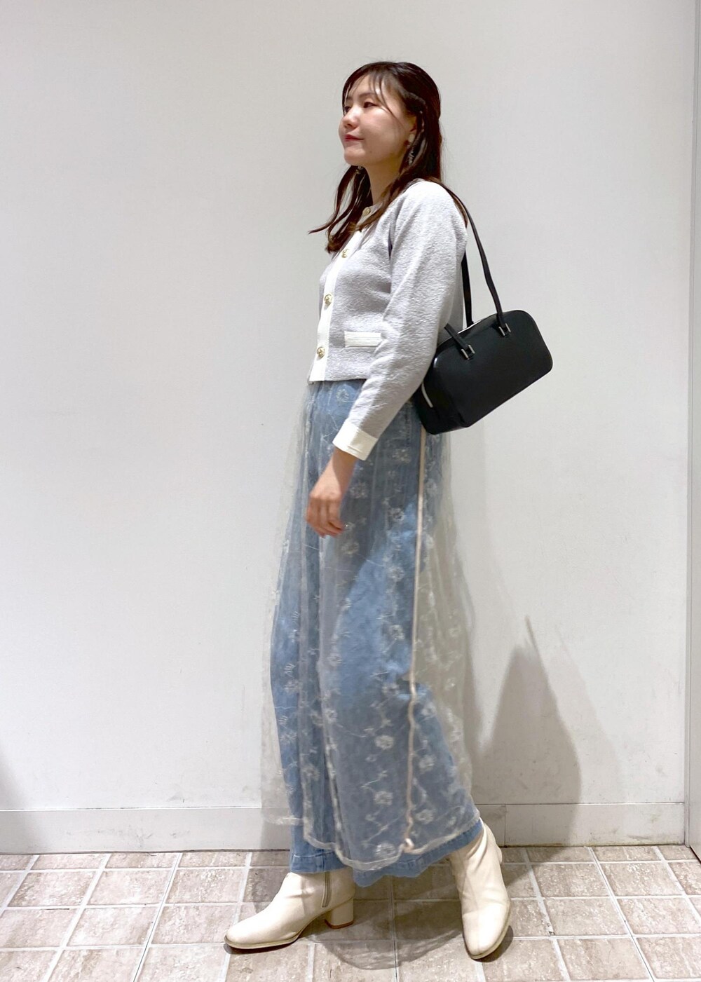 ブルー系のデニムパンツ、グレー系のカーディガン/ボレロ、ホワイト系のスカートを着用したレディースの秋コーディネートの5枚目の写真