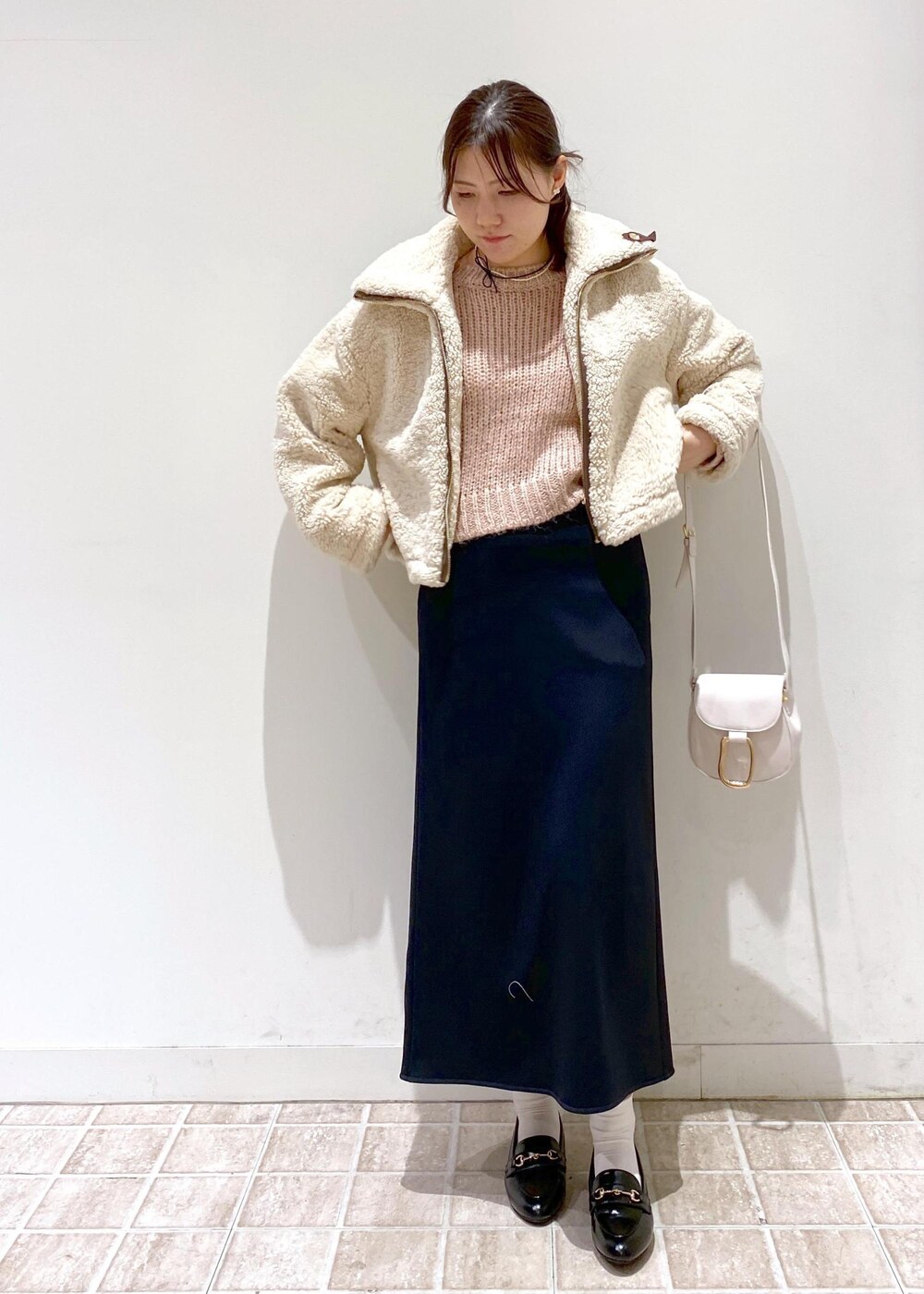 ブラック系のスカート、ベージュ系のムートンコート、ホワイト系のショルダーバッグを着用したレディースの冬コーディネートの2枚目の写真
