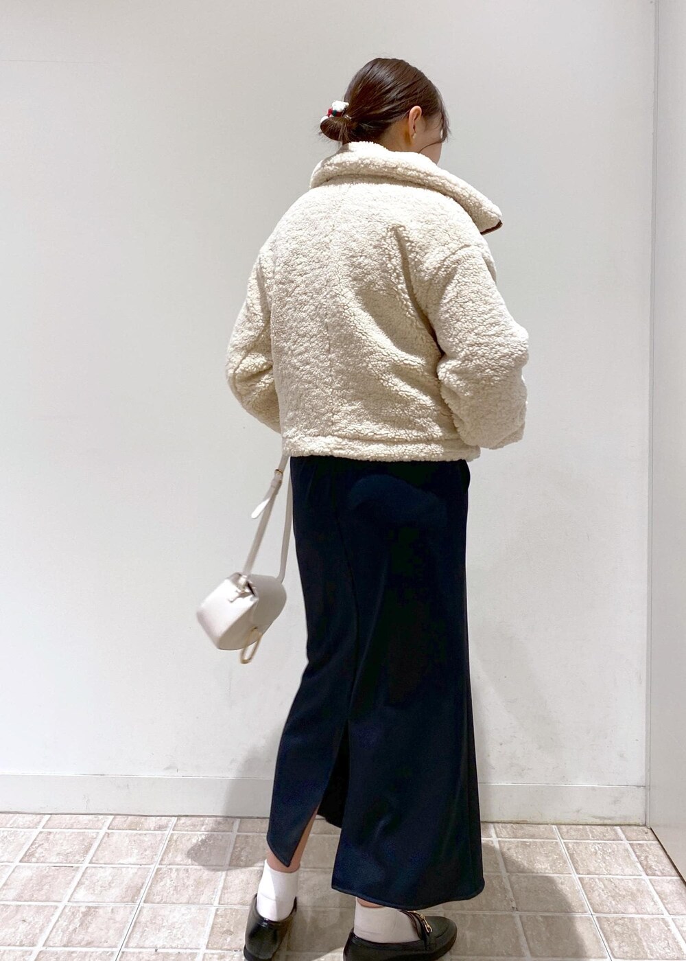 ブラック系のスカート、ベージュ系のムートンコート、ホワイト系のショルダーバッグを着用したレディースの冬コーディネートの7枚目の写真