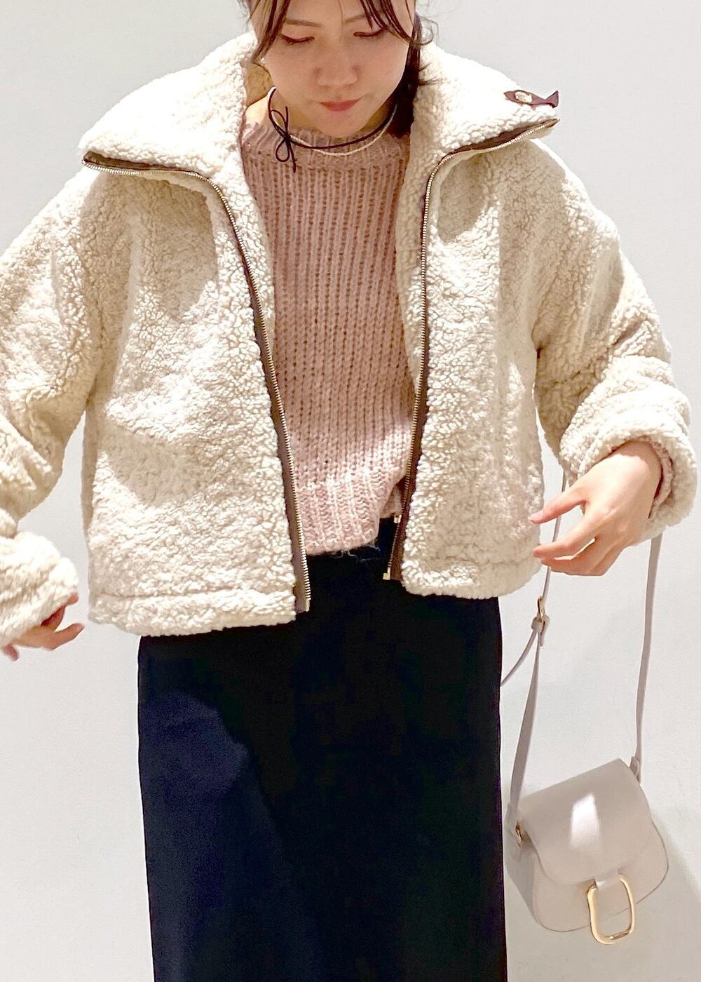 ブラック系のスカート、ベージュ系のムートンコート、ホワイト系のショルダーバッグを着用したレディースの冬コーディネートの6枚目の写真