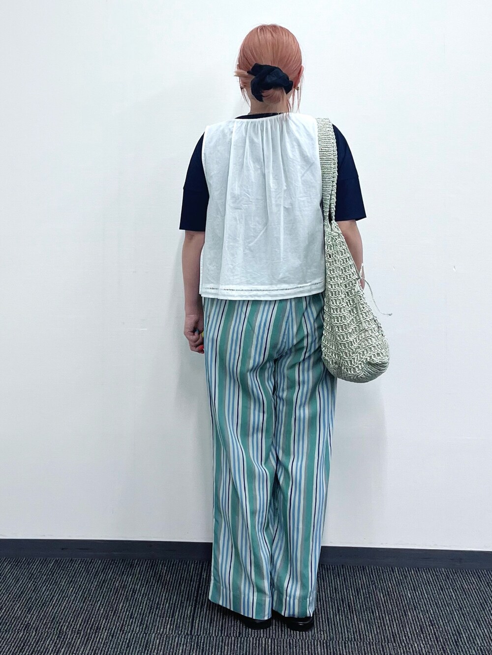 ホワイト系のベスト、グリーン系のその他パンツ、ゴールド系のかごバッグを着用したレディースの夏コーディネートの2枚目の写真