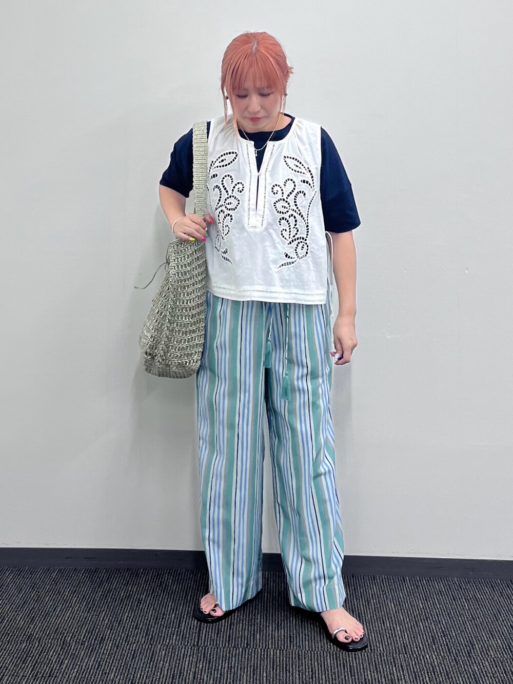 ホワイト系のベスト、グリーン系のその他パンツ、ゴールド系のかごバッグを着用したレディースの夏コーディネートの5枚目の写真