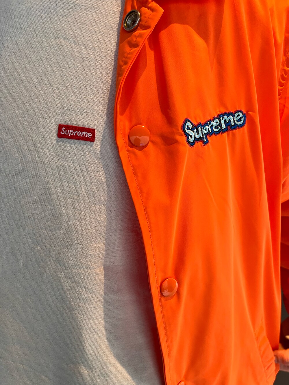 オレンジ系のナイロンジャケット、ホワイト系のスウェット、ホワイト系のデニムパンツを着用したメンズの秋コーディネートの2枚目の写真