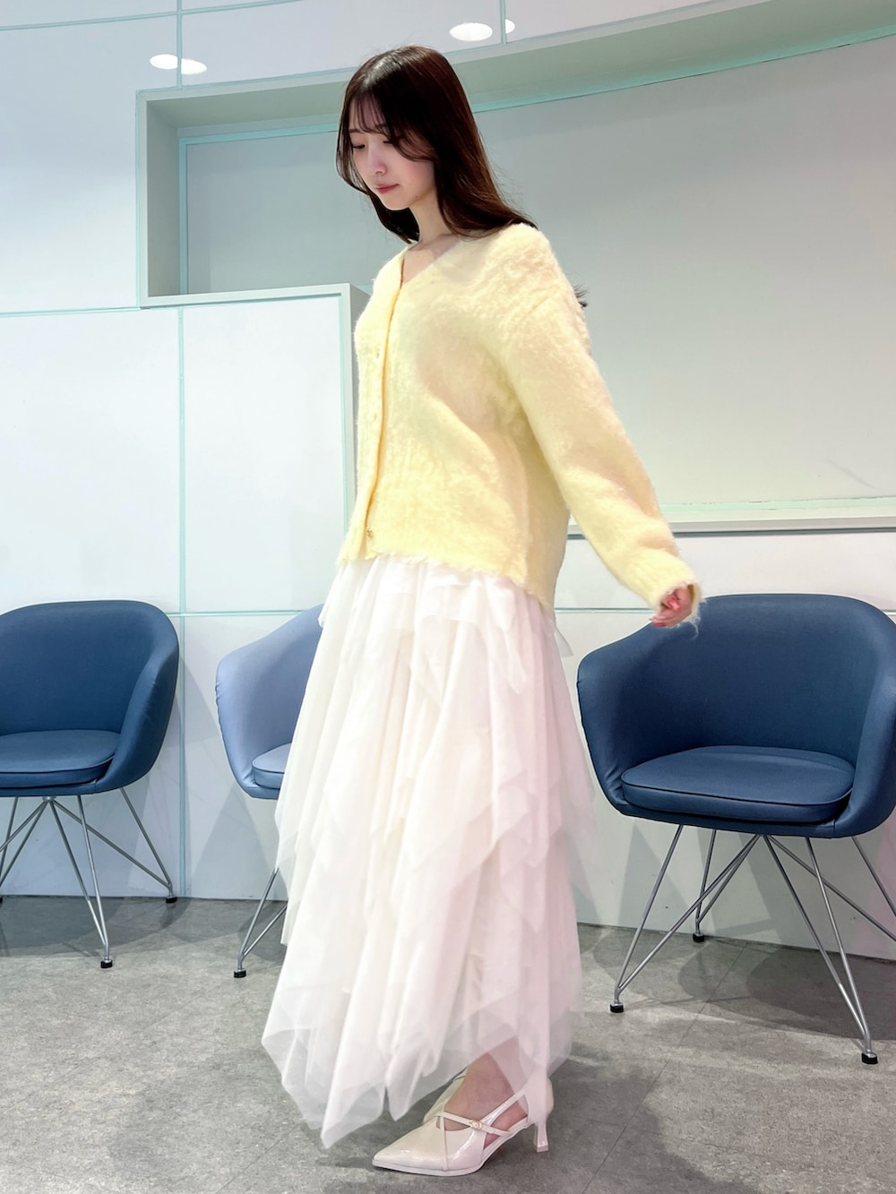 イエロー系のカーディガン/ボレロ、ホワイト系のスカート、ホワイト系のパンプスを着用したレディースの冬コーディネートの2枚目の写真