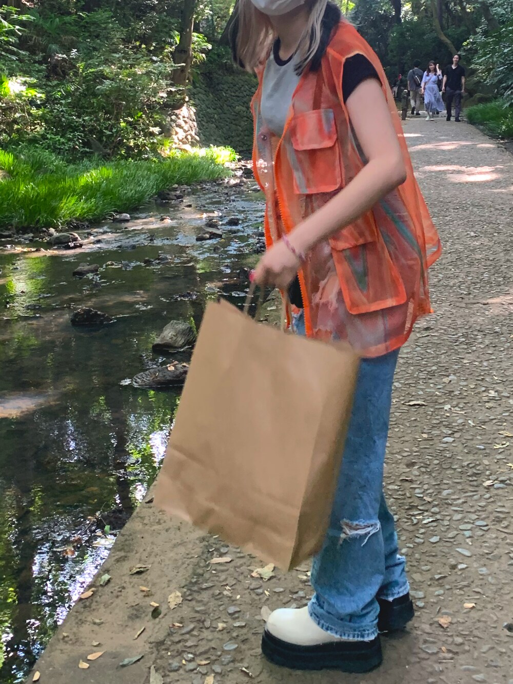 オレンジ系のベスト、ブルー系のデニムパンツ、ホワイト系のブーツを着用したレディースの秋コーディネートの2枚目の写真