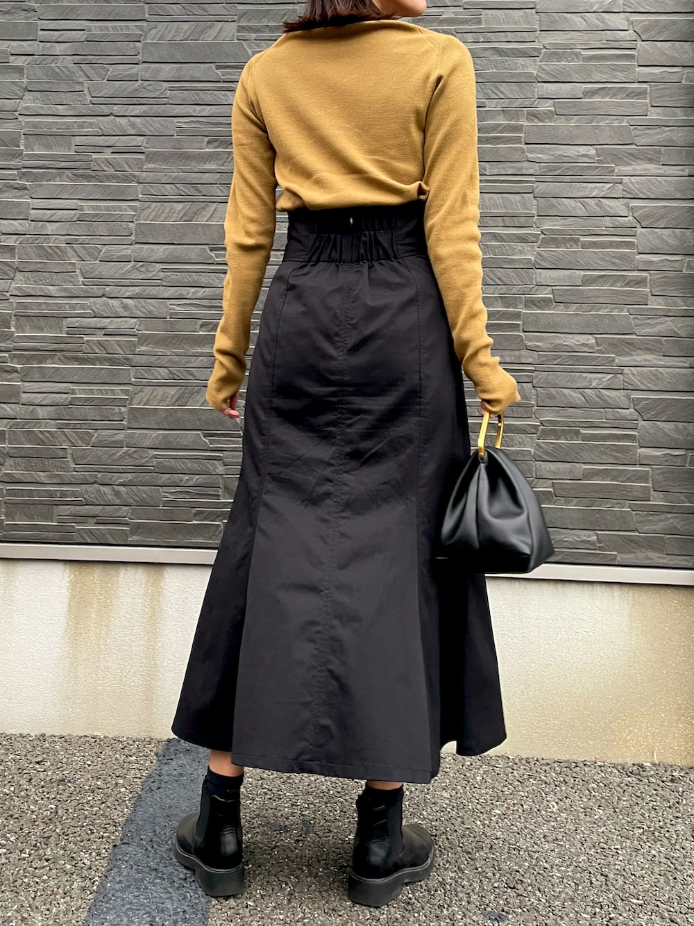 イエロー系のニット/セーター、ブラック系のスカート、ブラック系のハンドバッグを着用したレディースの秋コーディネートの2枚目の写真