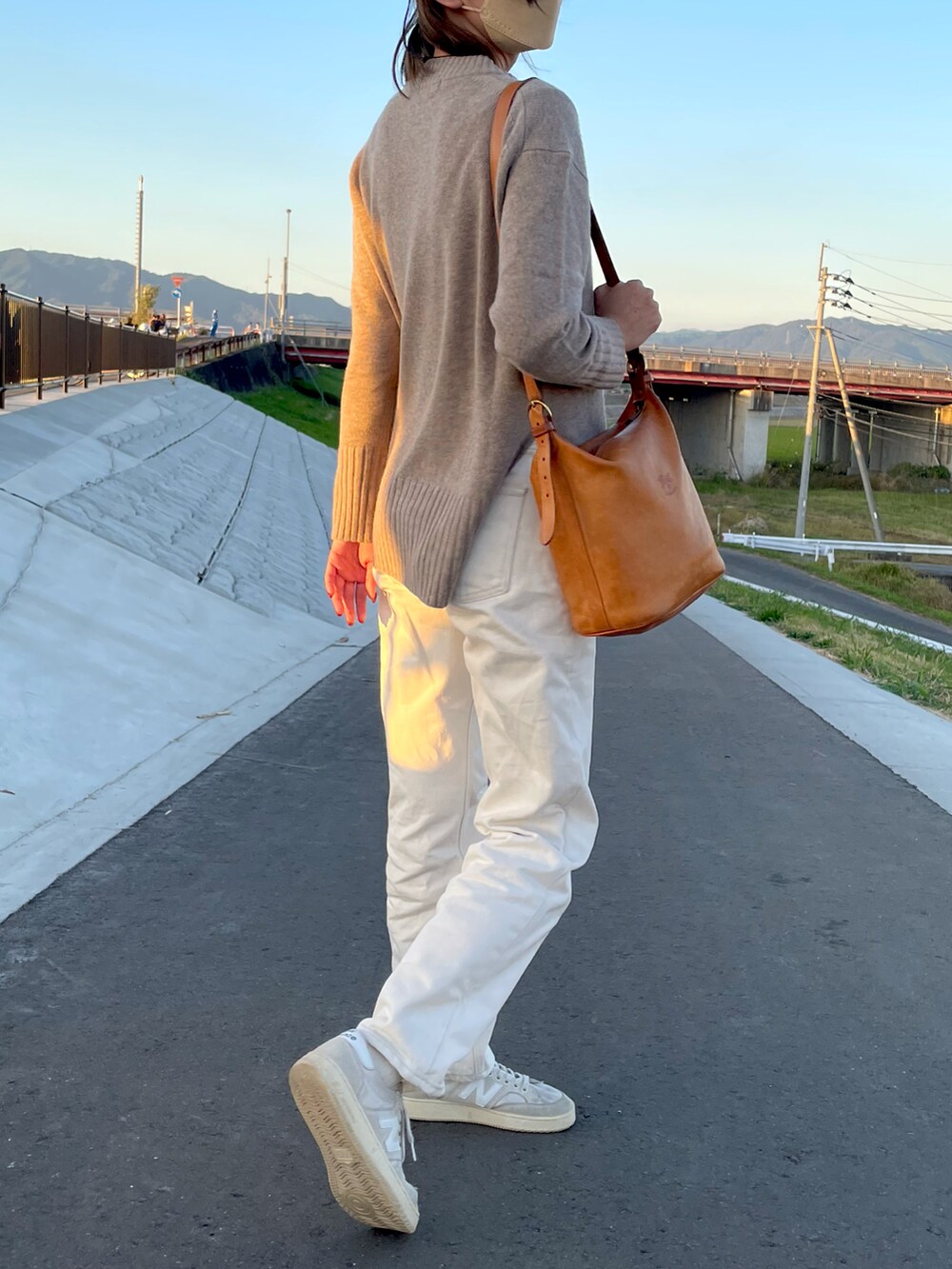 ベージュ系のニット/セーター、オレンジ系のショルダーバッグ、ホワイト系のデニムパンツを着用したレディースの秋コーディネートの2枚目の写真