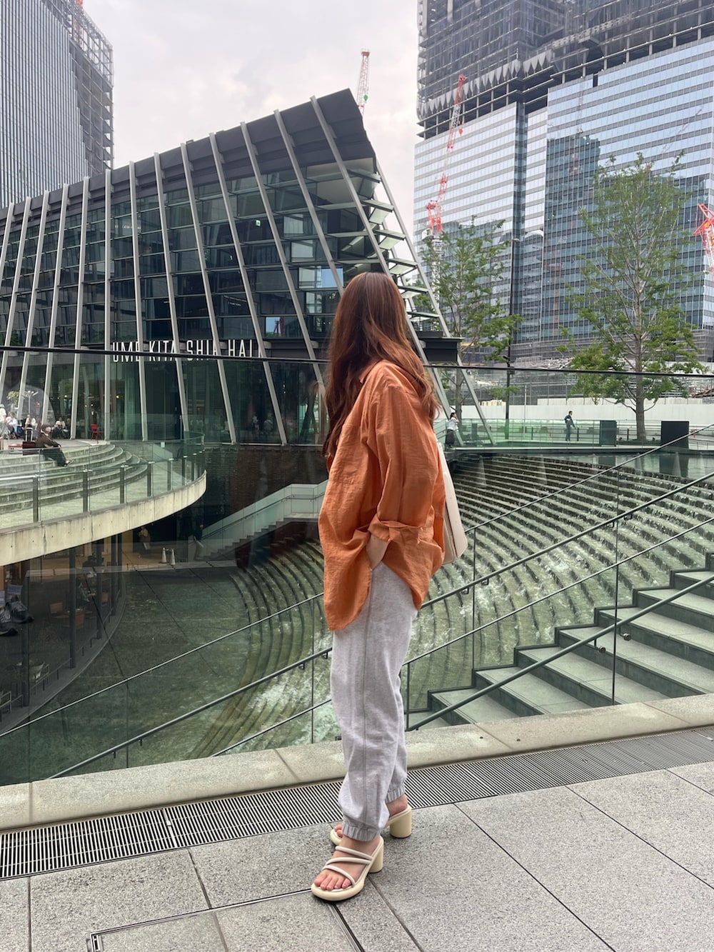 オレンジ系のシャツ/ブラウス、ホワイト系のサンダル、ベージュ系のショルダーバッグを着用したレディースの春コーディネートの2枚目の写真