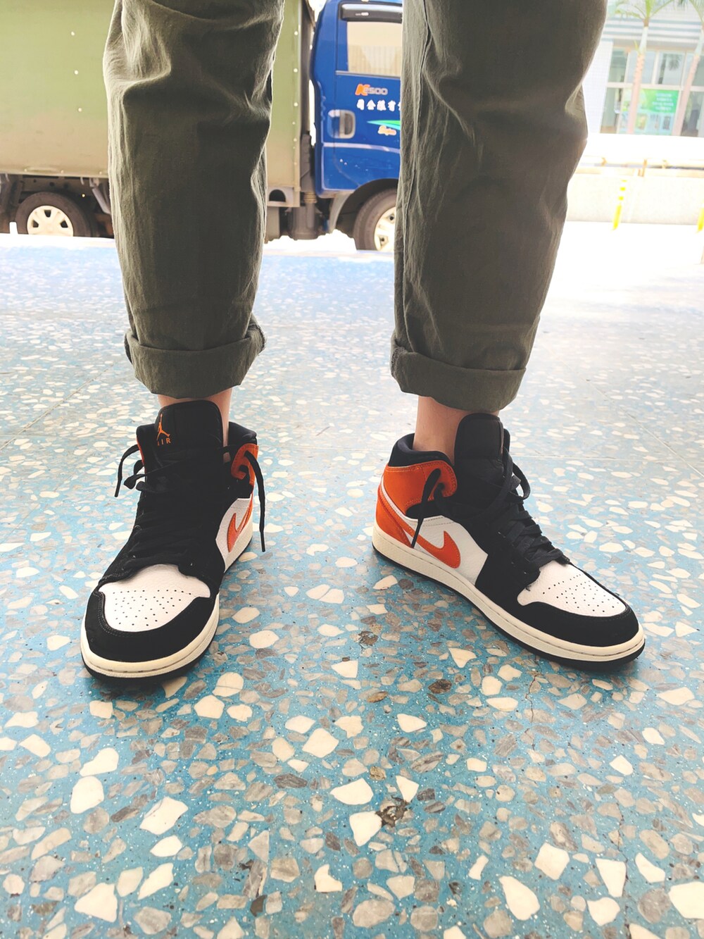 グリーン系のチノパンツ、ブラック系のTシャツ/カットソー、オレンジ系のスニーカーを着用したメンズの夏コーディネートの2枚目の写真