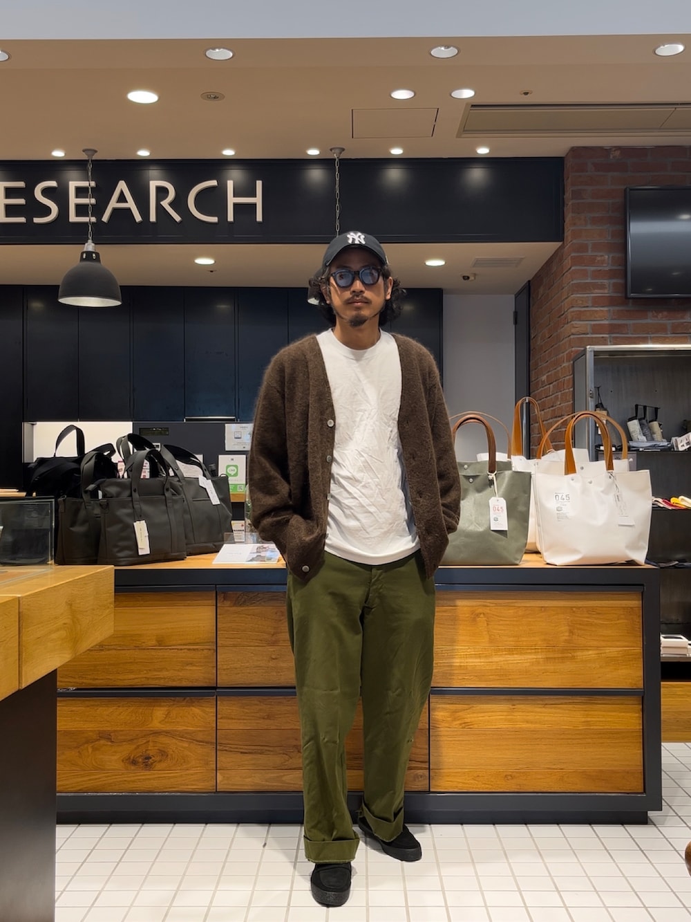 ブラウン系のカーディガン/ボレロ、ブラック系のローファー、ブルー系のキャップを着用したメンズの秋コーディネートの5枚目の写真