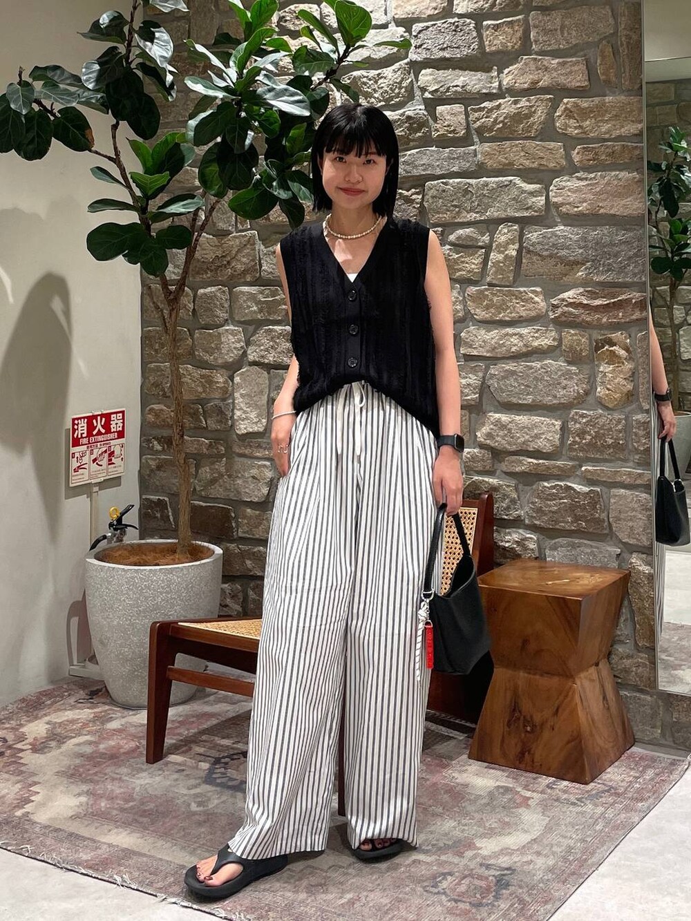 ブラック系のベスト、ブラック系のハンドバッグ、ホワイト系のその他パンツを着用したレディースの夏コーディネートの2枚目の写真