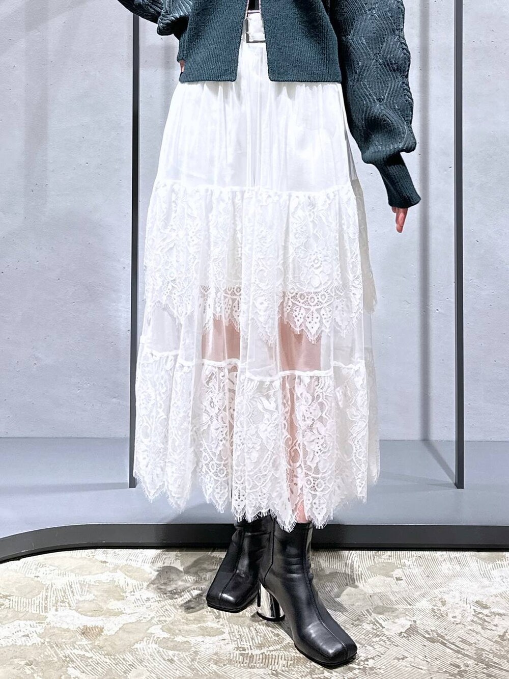 ブラック系のブーツ、グリーン系のカーディガン/ボレロ、ホワイト系のスカートを着用したレディースの秋コーディネートの6枚目の写真