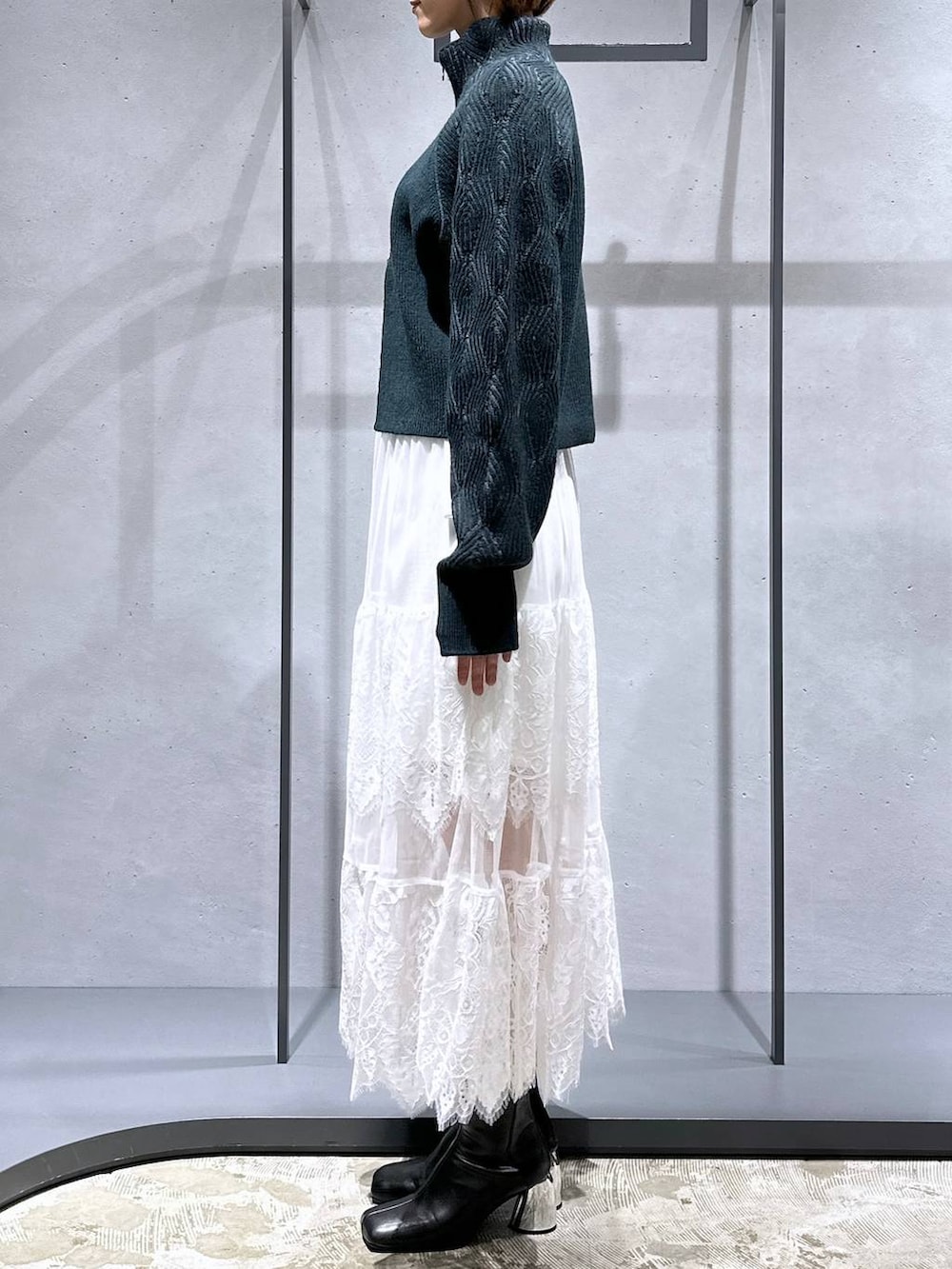 ブラック系のブーツ、グリーン系のカーディガン/ボレロ、ホワイト系のスカートを着用したレディースの秋コーディネートの2枚目の写真