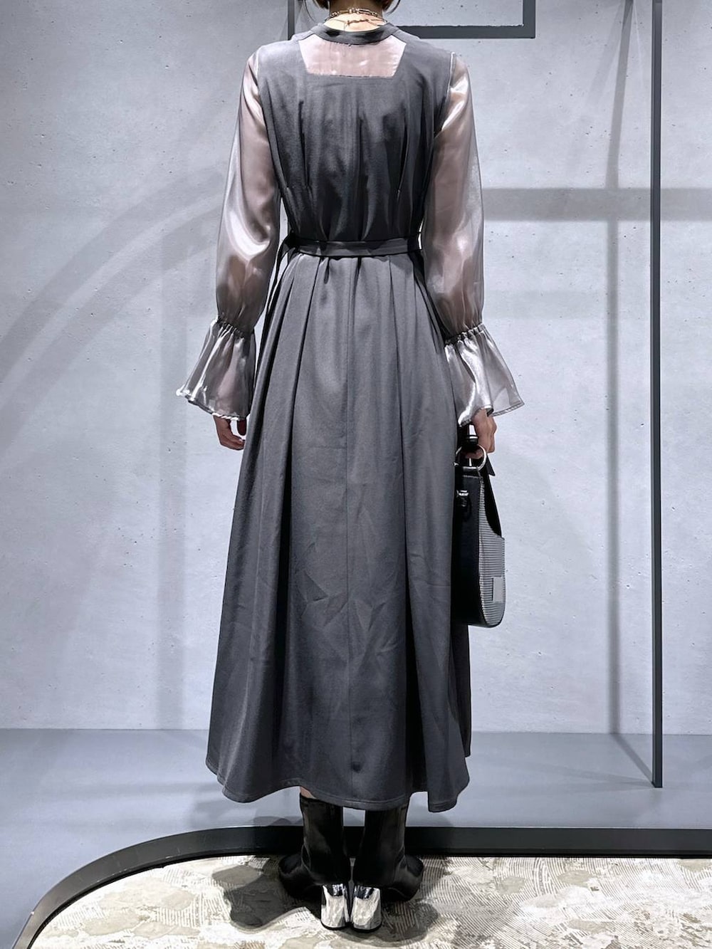 シルバー系のハンドバッグ、ブラック系のブーツ、グレー系のドレスを着用したレディースの秋コーディネートの4枚目の写真