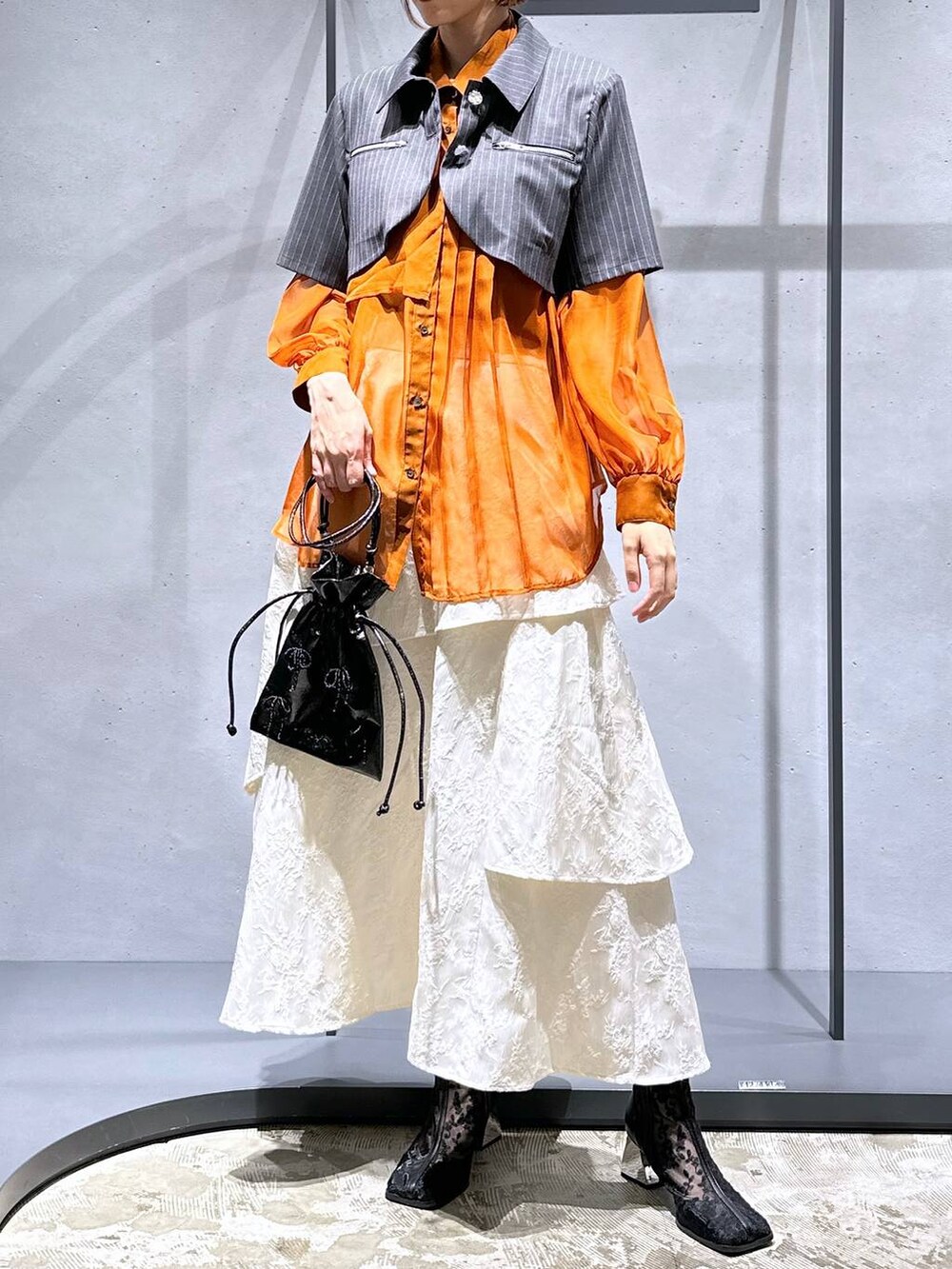 オレンジ系のシャツ/ブラウス、ホワイト系のスカート、ブラック系のブーツを着用したレディースの夏コーディネートの5枚目の写真