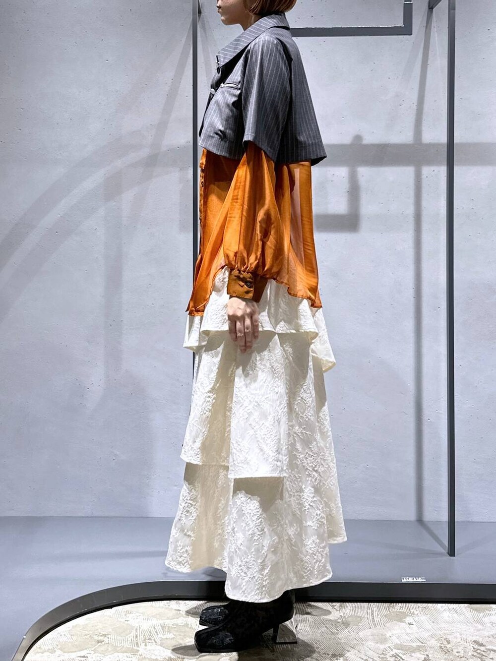 オレンジ系のシャツ/ブラウス、ホワイト系のスカート、ブラック系のブーツを着用したレディースの夏コーディネートの2枚目の写真