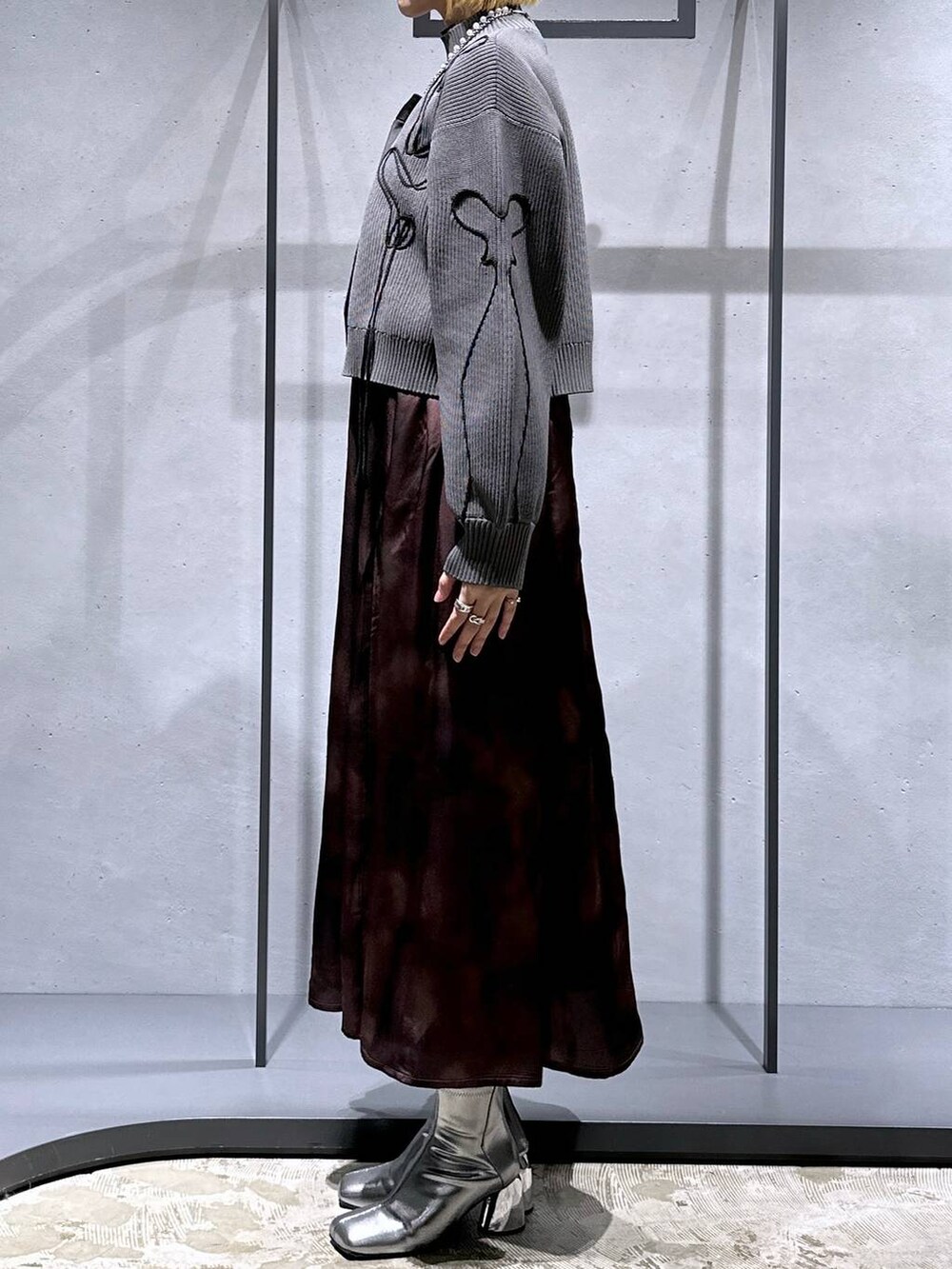 ブラック系のネクタイ、シルバー系のブーツ、グレー系のニット/セーターを着用したレディースの冬コーディネートの2枚目の写真