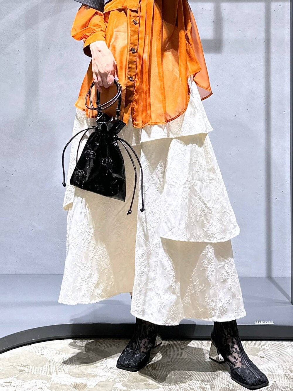 オレンジ系のシャツ/ブラウス、ホワイト系のスカート、ブラック系のブーツを着用したレディースの夏コーディネートの7枚目の写真