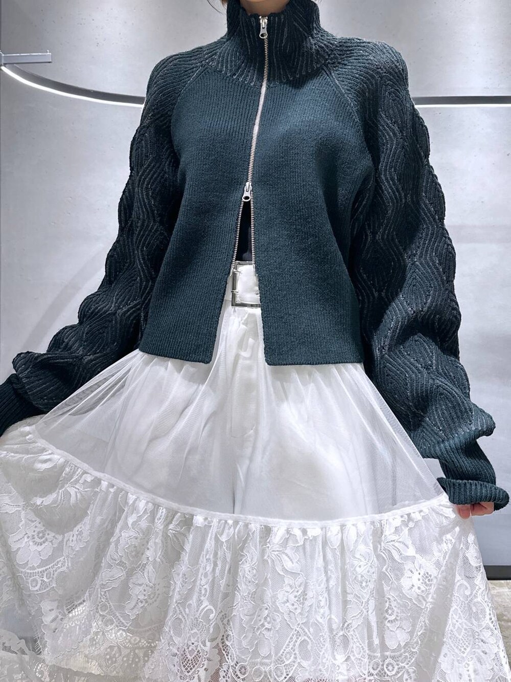 ブラック系のブーツ、グリーン系のカーディガン/ボレロ、ホワイト系のスカートを着用したレディースの秋コーディネートの5枚目の写真