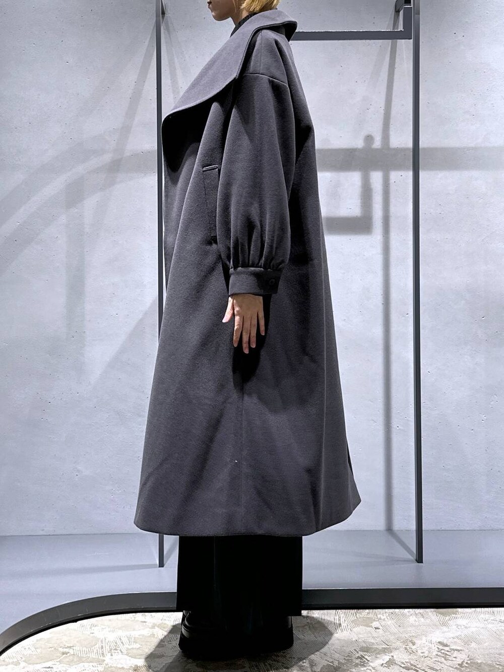 グレー系のチェスターコート、ブラック系のニット/セーター、グリーン系のシャツ/ブラウスを着用したレディースの秋コーディネートの2枚目の写真